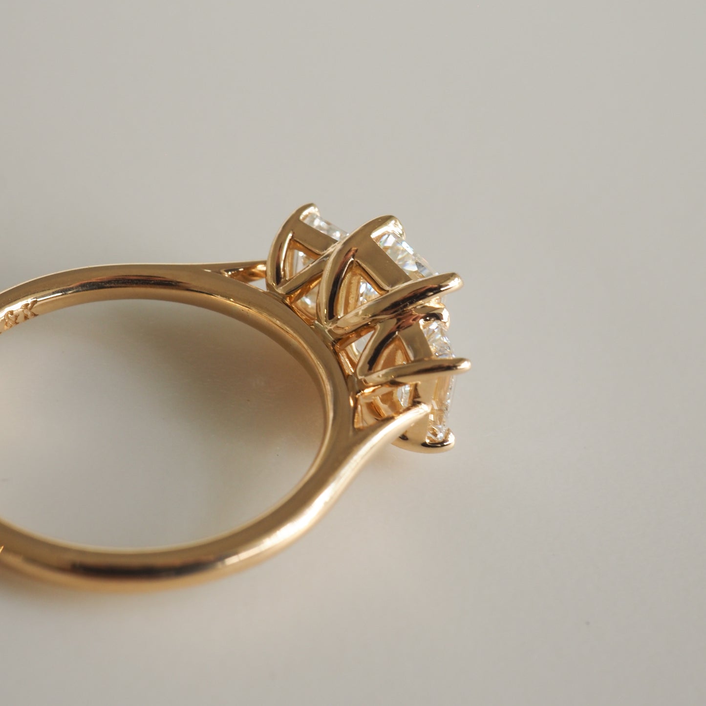 Gold engagement ring with a trio of sparkling diamonds set in elegant prongs, showcased on a smooth white surface.