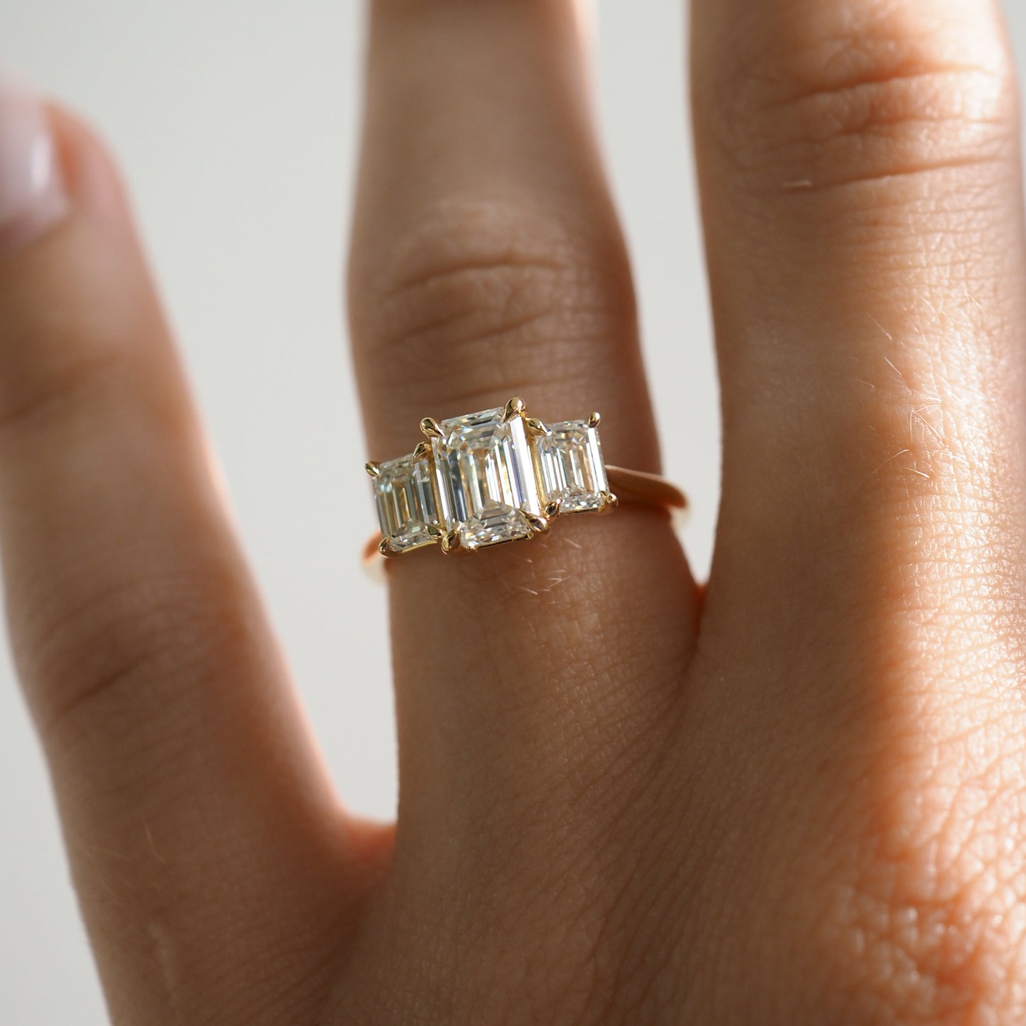 Elegant gold ring with three emerald-cut diamonds on a finger, showcasing luxury jewellery design.