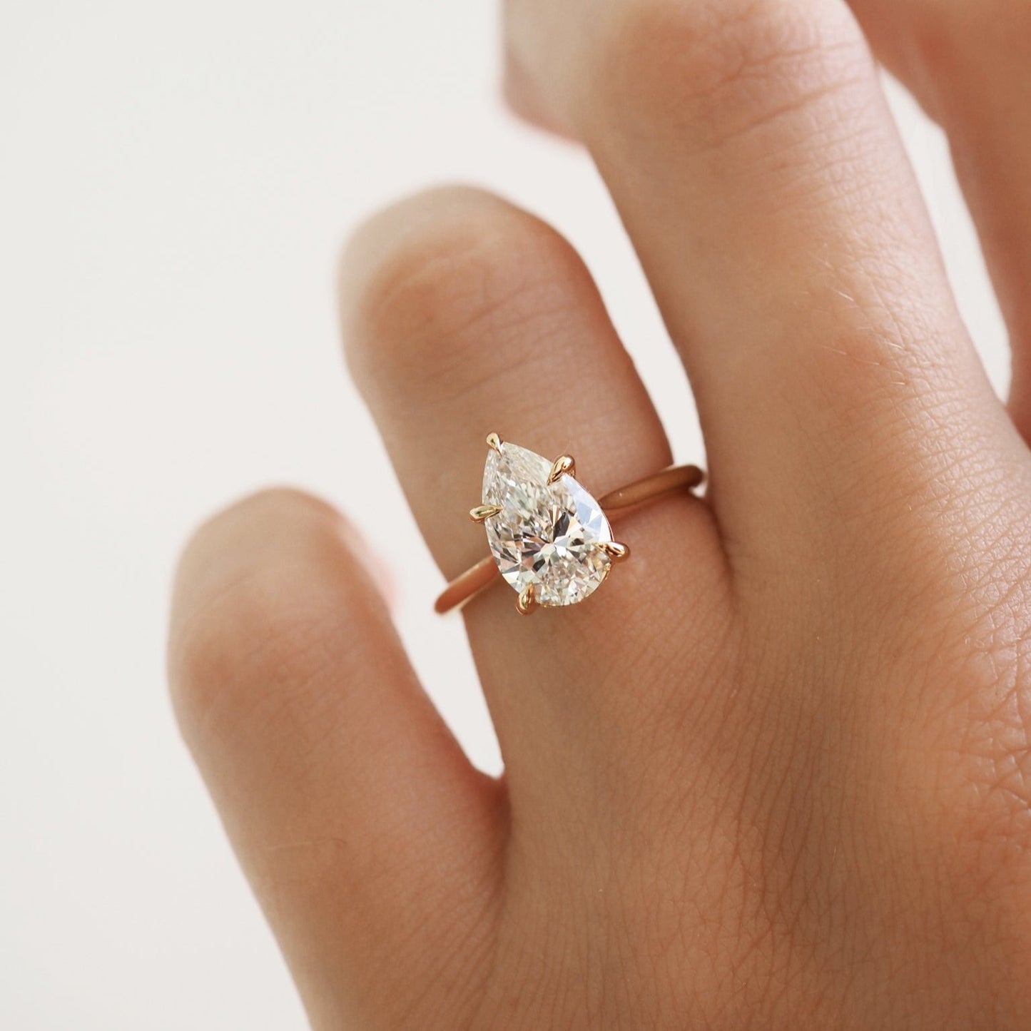 A hand wearing a gold ring with a large pear-shaped diamond, showcasing elegant luxury jewellery design.