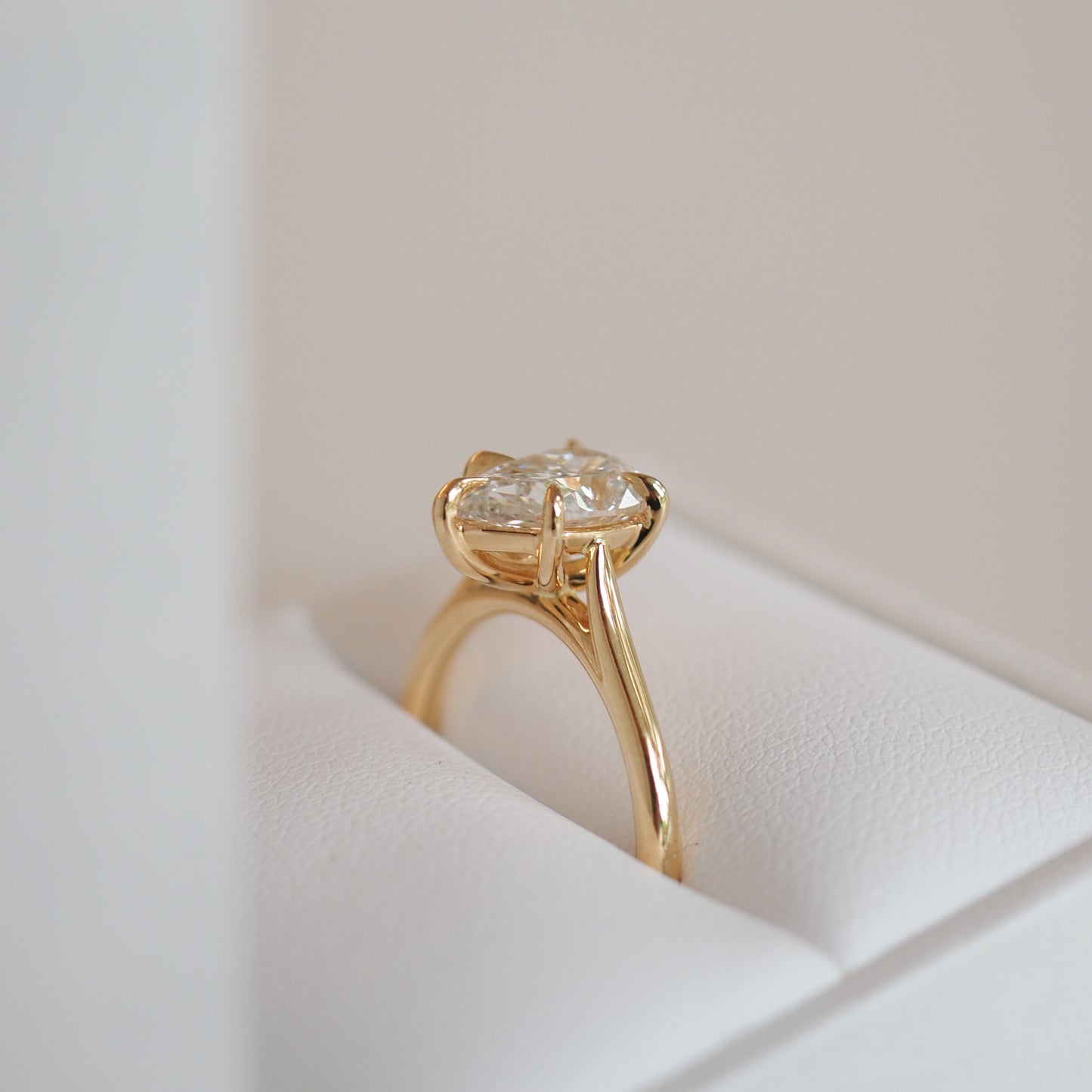 Gold engagement ring with a solitaire diamond on a white cushion. Elegant and luxurious jewellery piece displayed in soft lighting.