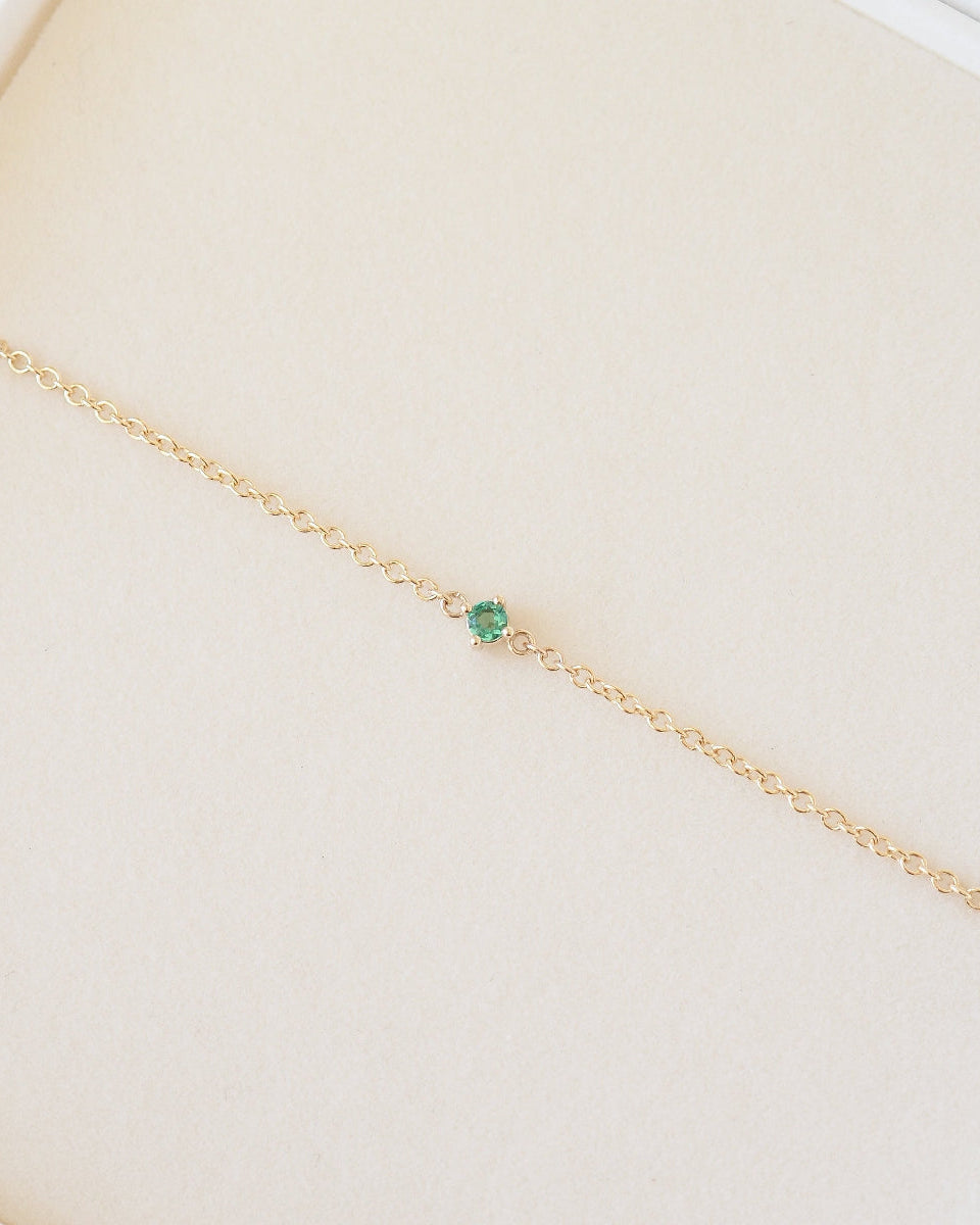 Gold bracelet with a green gemstone on a beige background
