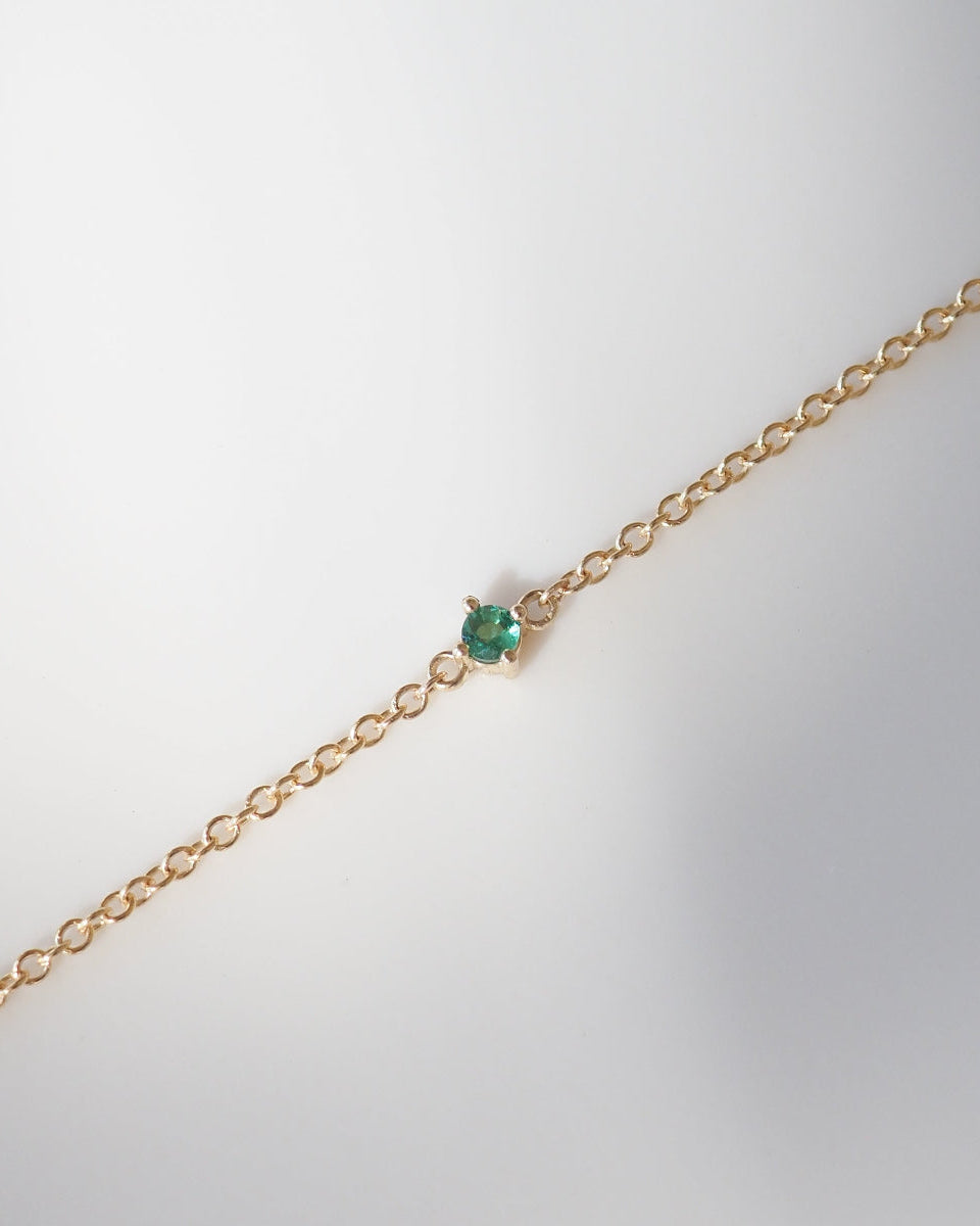 Gold bracelet with a green gemstone on a light gray background