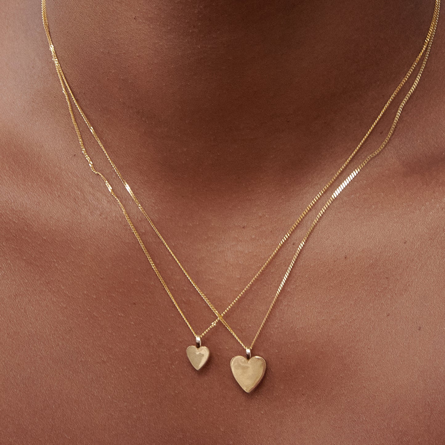 Close-up of a woman wearing two gold heart pendants on delicate chains against her skin, showcasing luxury jewellery design.