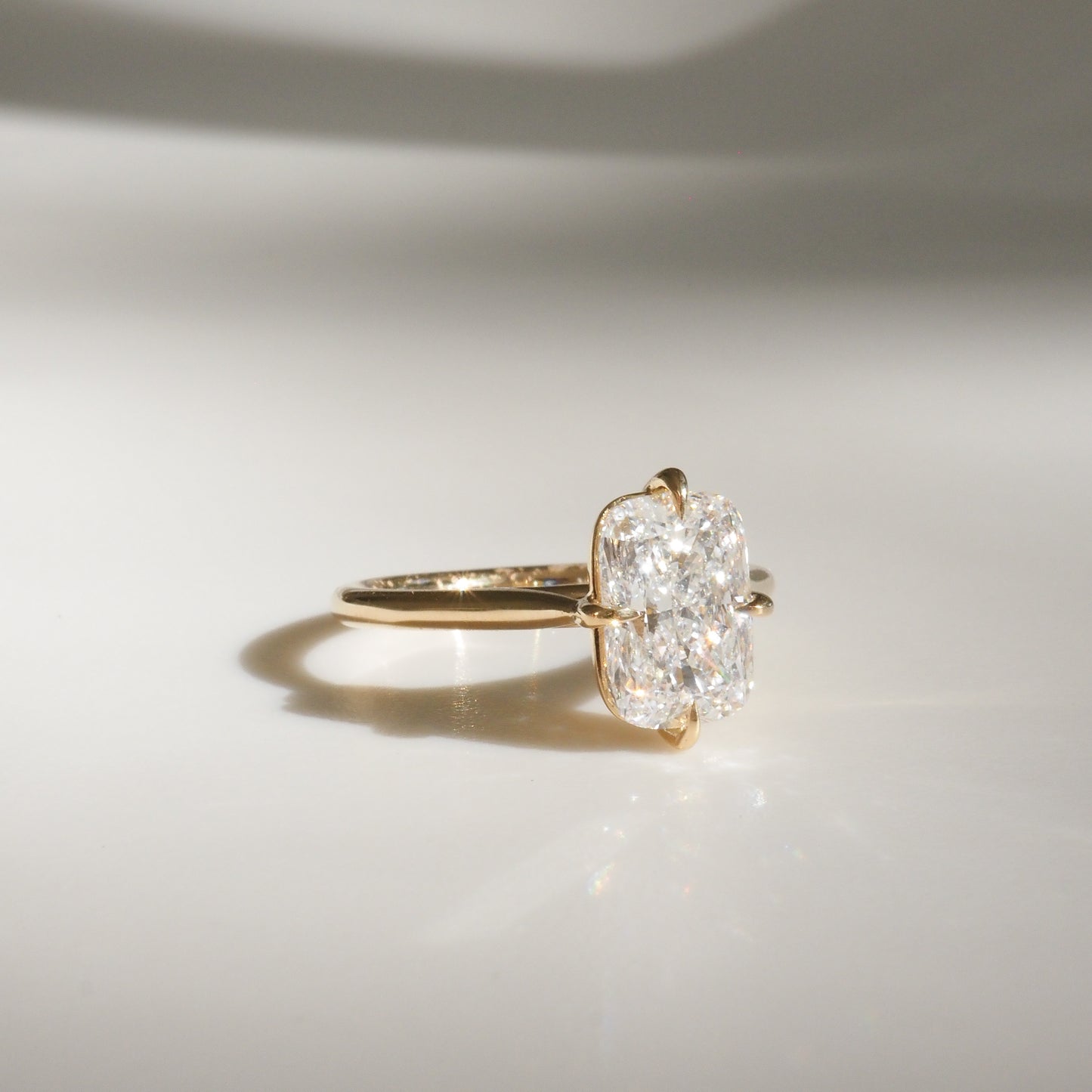 Gold ring with a cushion-cut diamond on a light background. The diamond sparkles, showcasing its clarity and brilliance. Luxurious jewellery.