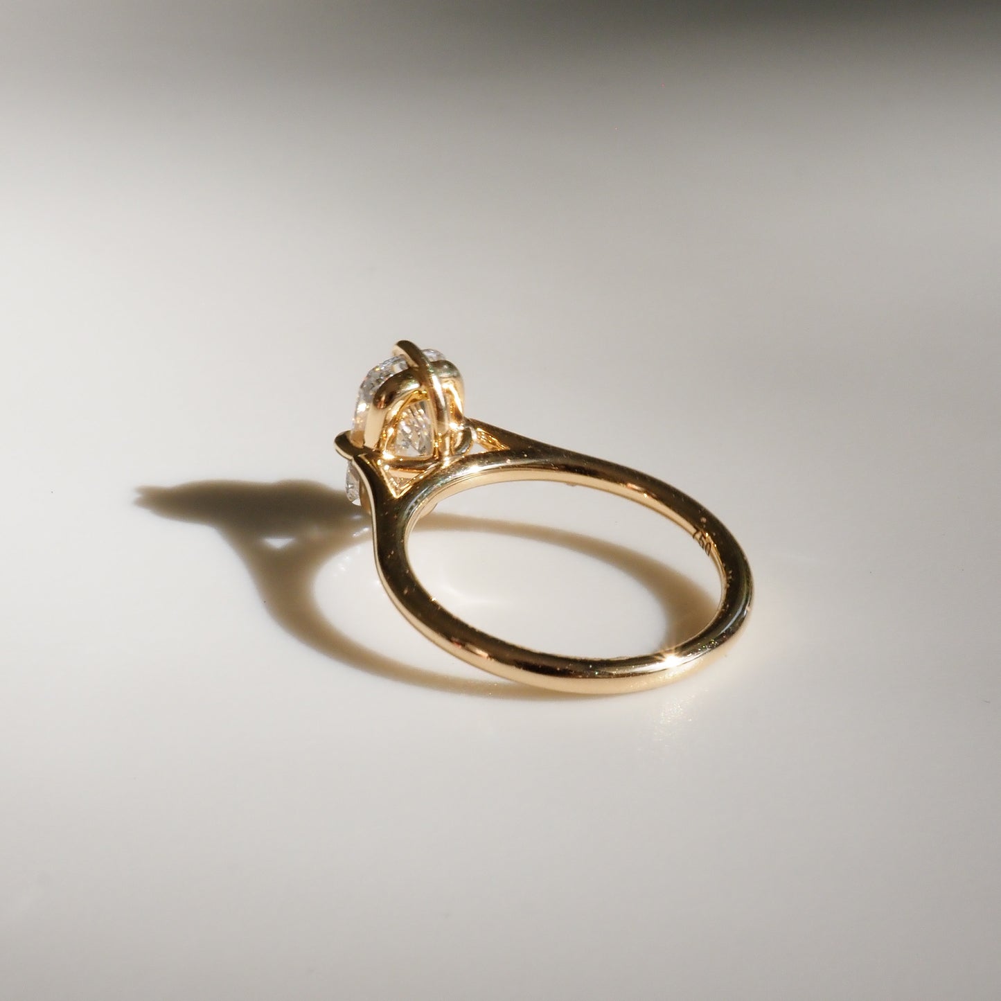 Gold engagement ring with a diamond solitaire set in a classic prong setting, casting a delicate shadow on a white background.