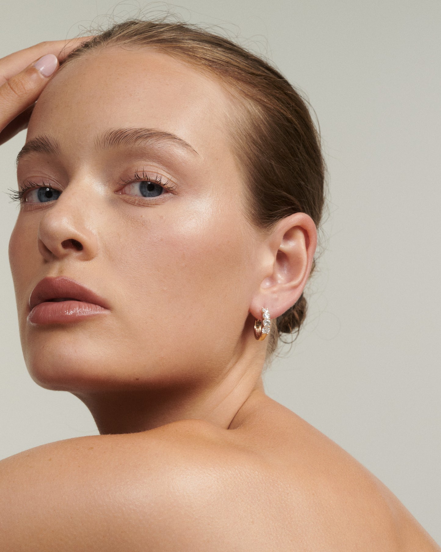 Close-up of a woman's face wearing earrings with a neutral background