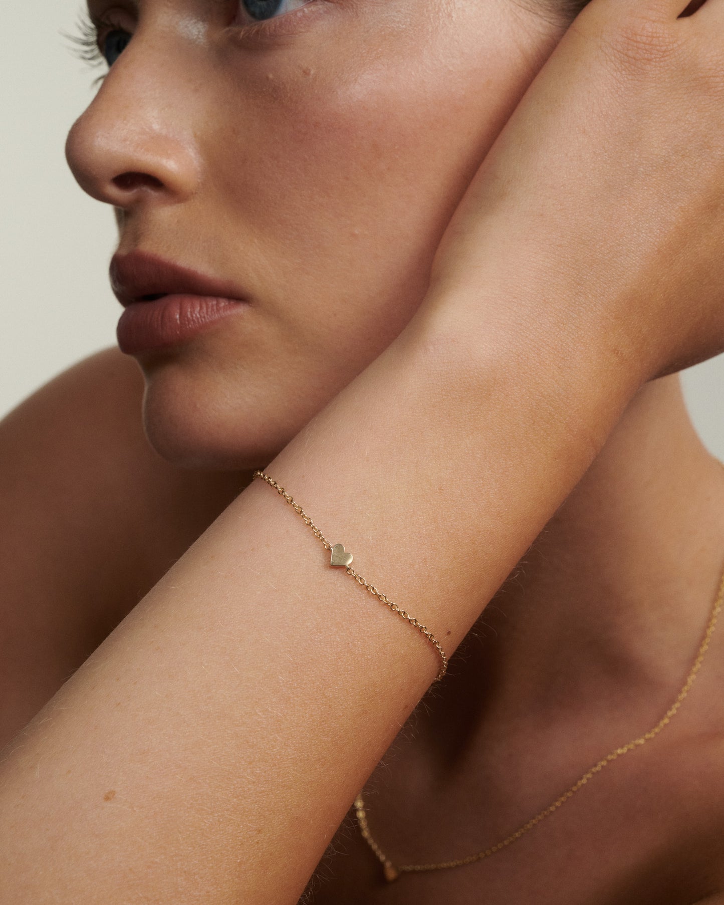 Close-up of a woman's arm wearing a delicate gold bracelet with a heart charm.