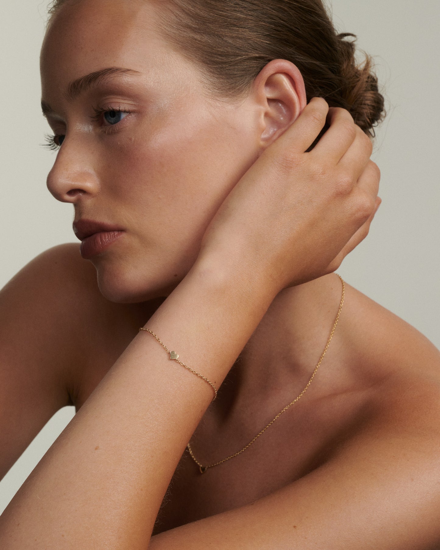 Woman wearing a delicate gold necklace and bracelet against a neutral background