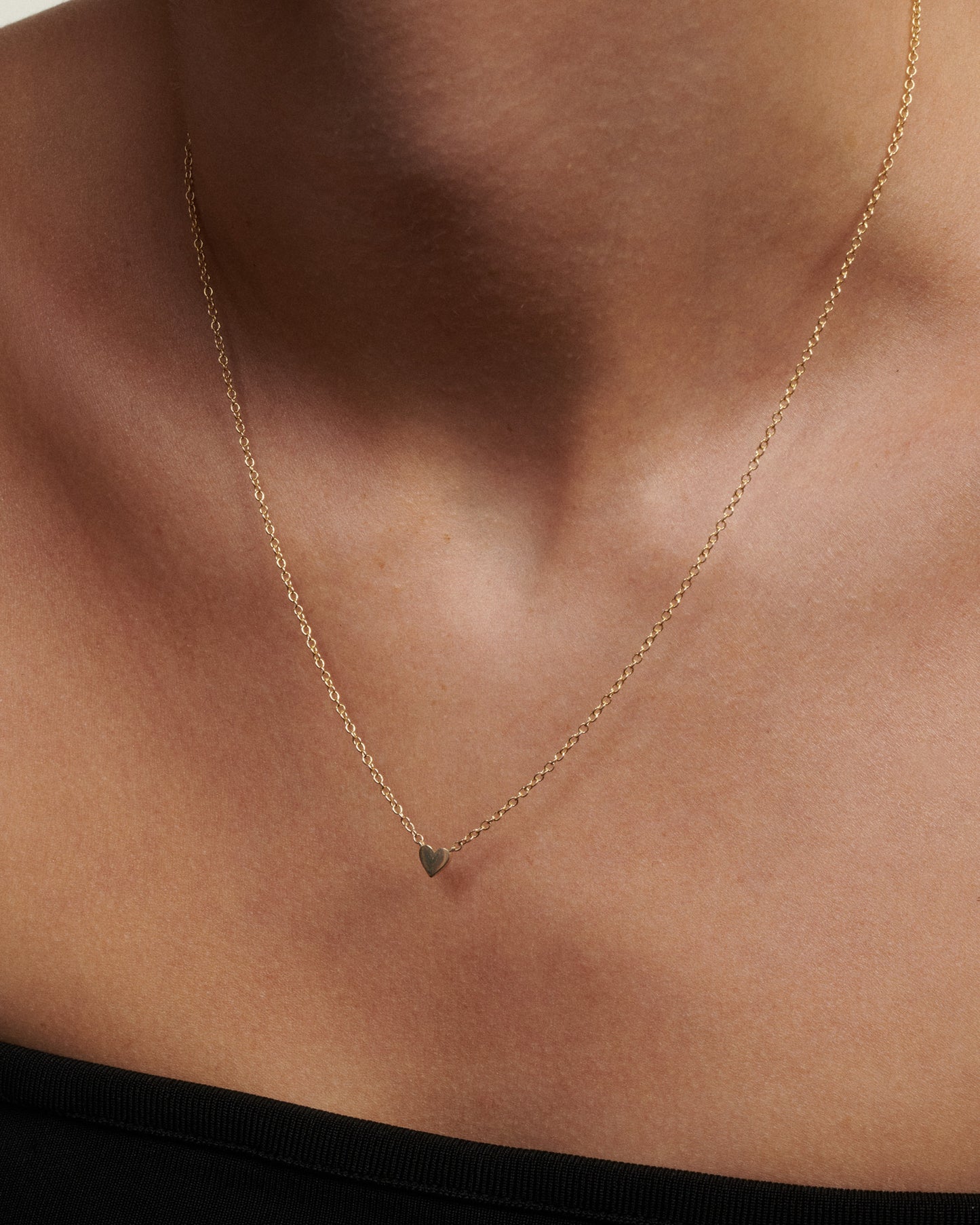 Gold necklace with a small green pendant on a person's neck