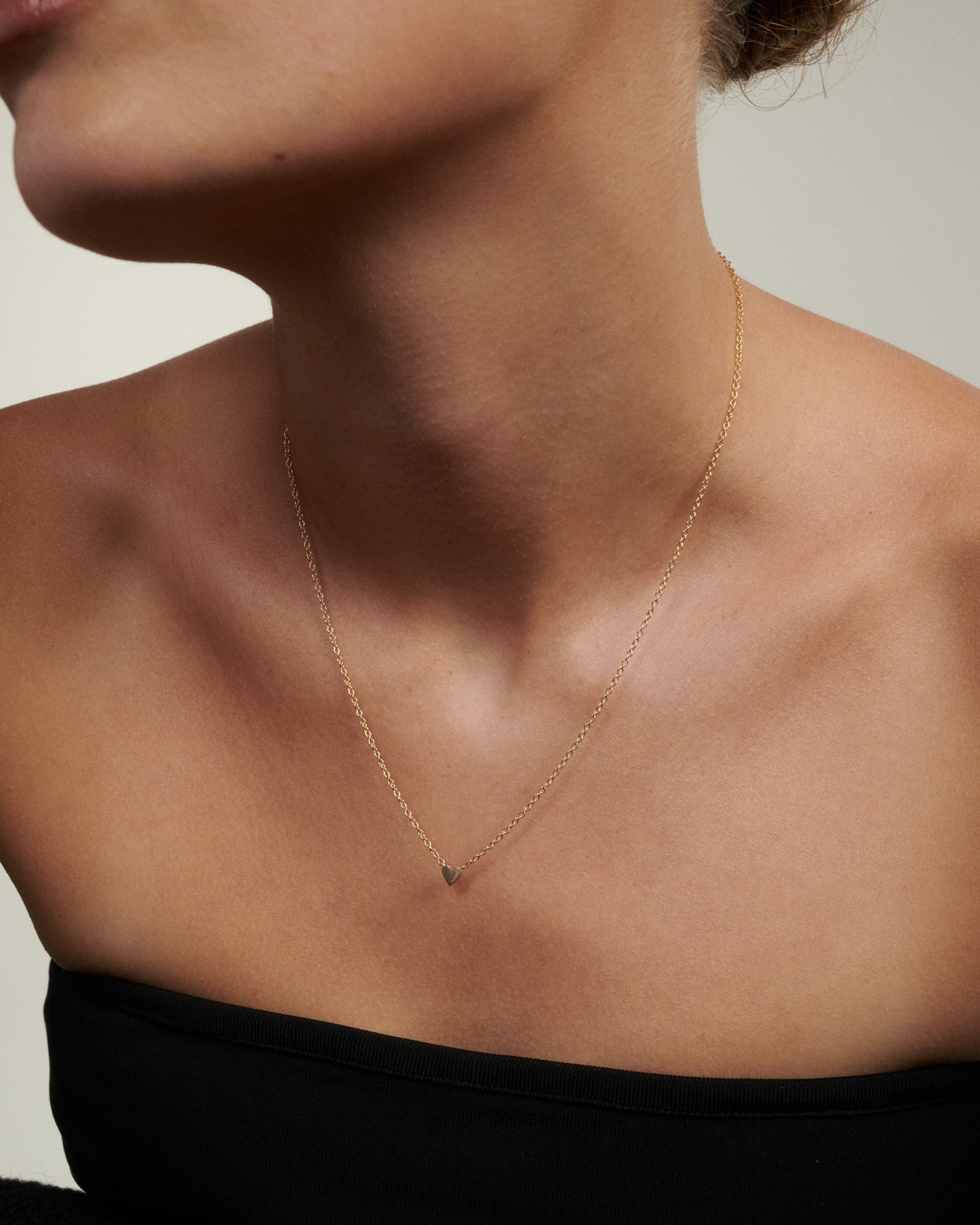 Close-up of a person wearing a delicate gold necklace with a small pendant on a neutral background