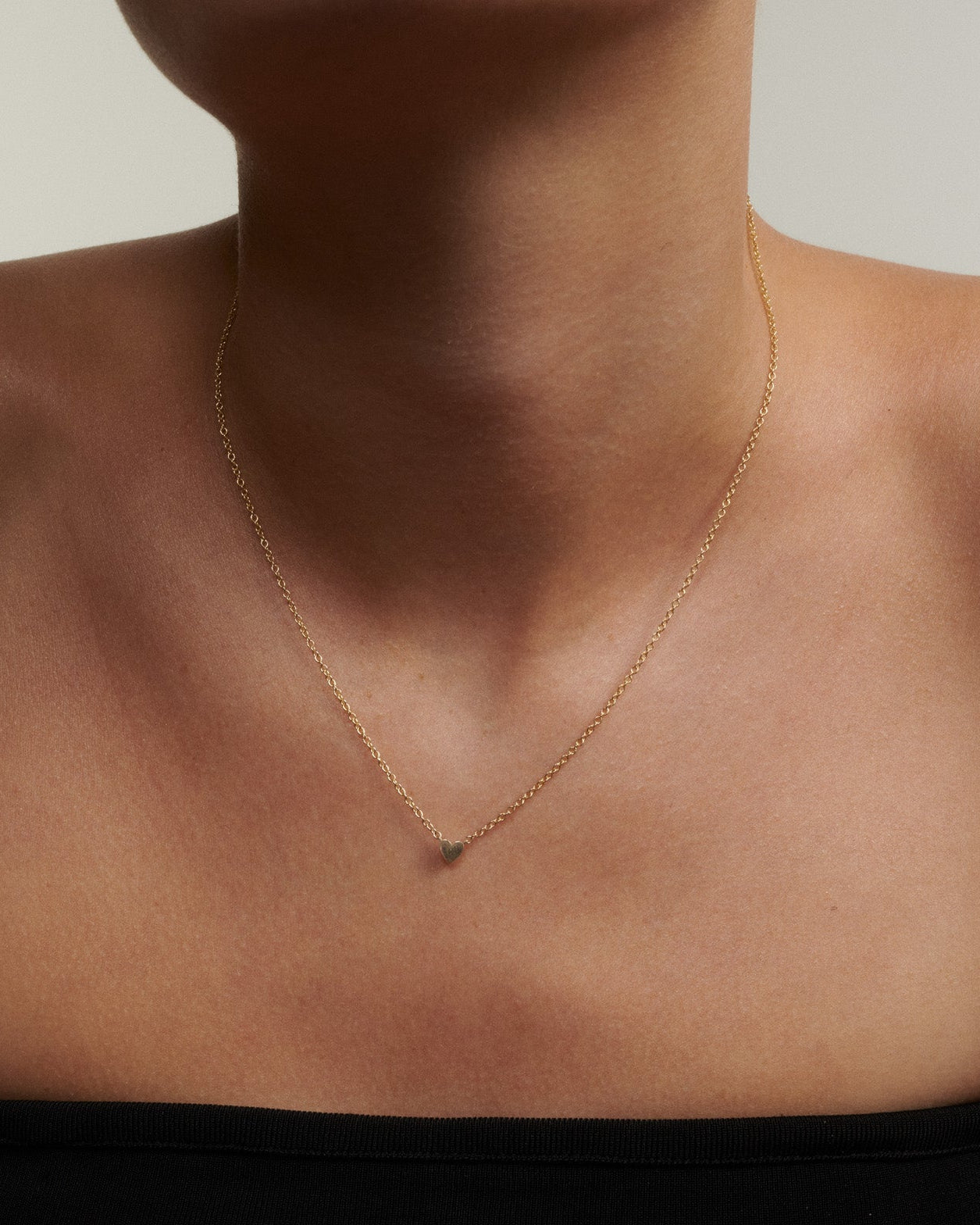 Gold necklace on a person wearing a black top against a neutral background