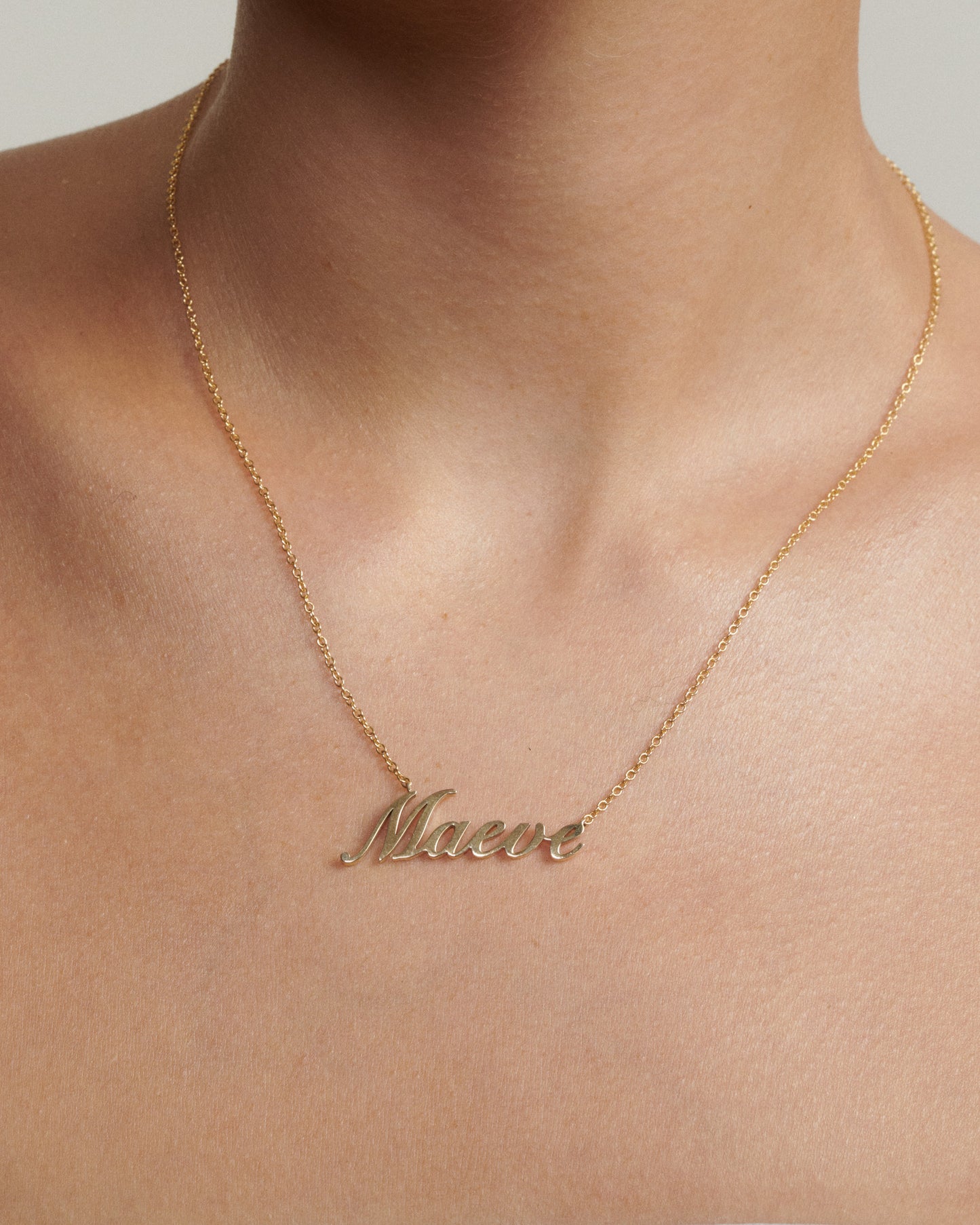 Gold necklace with 'Maeve' pendant on a neutral background