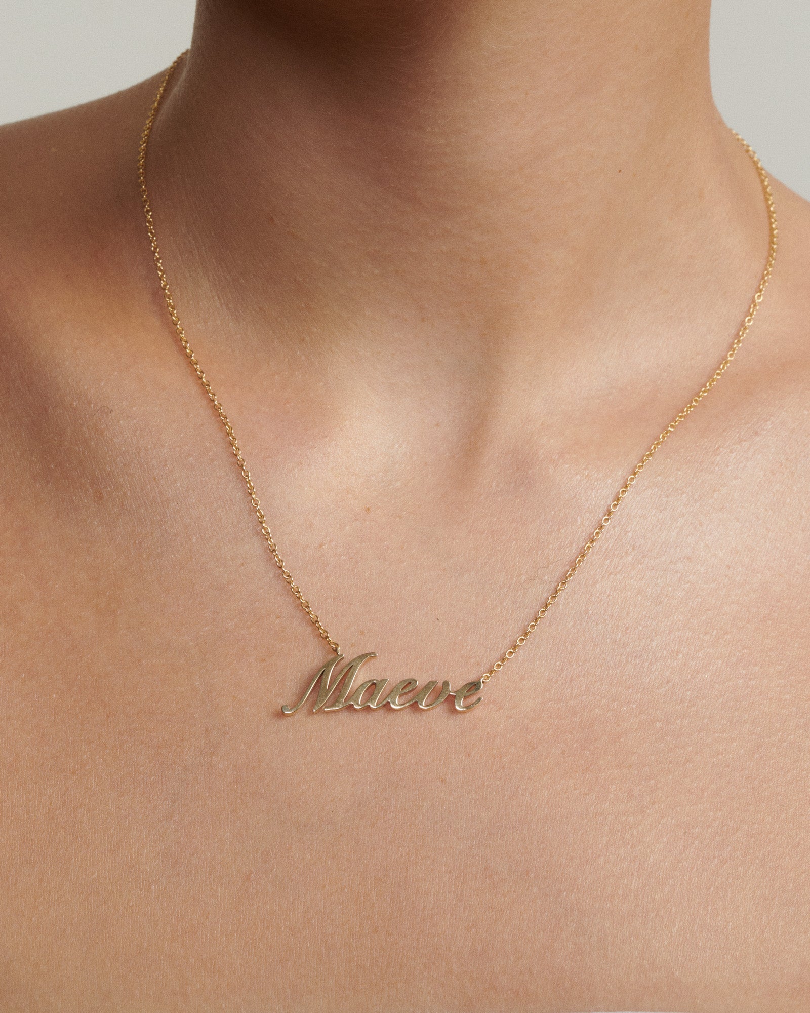 Gold necklace with 'Maeve' pendant on a neutral background