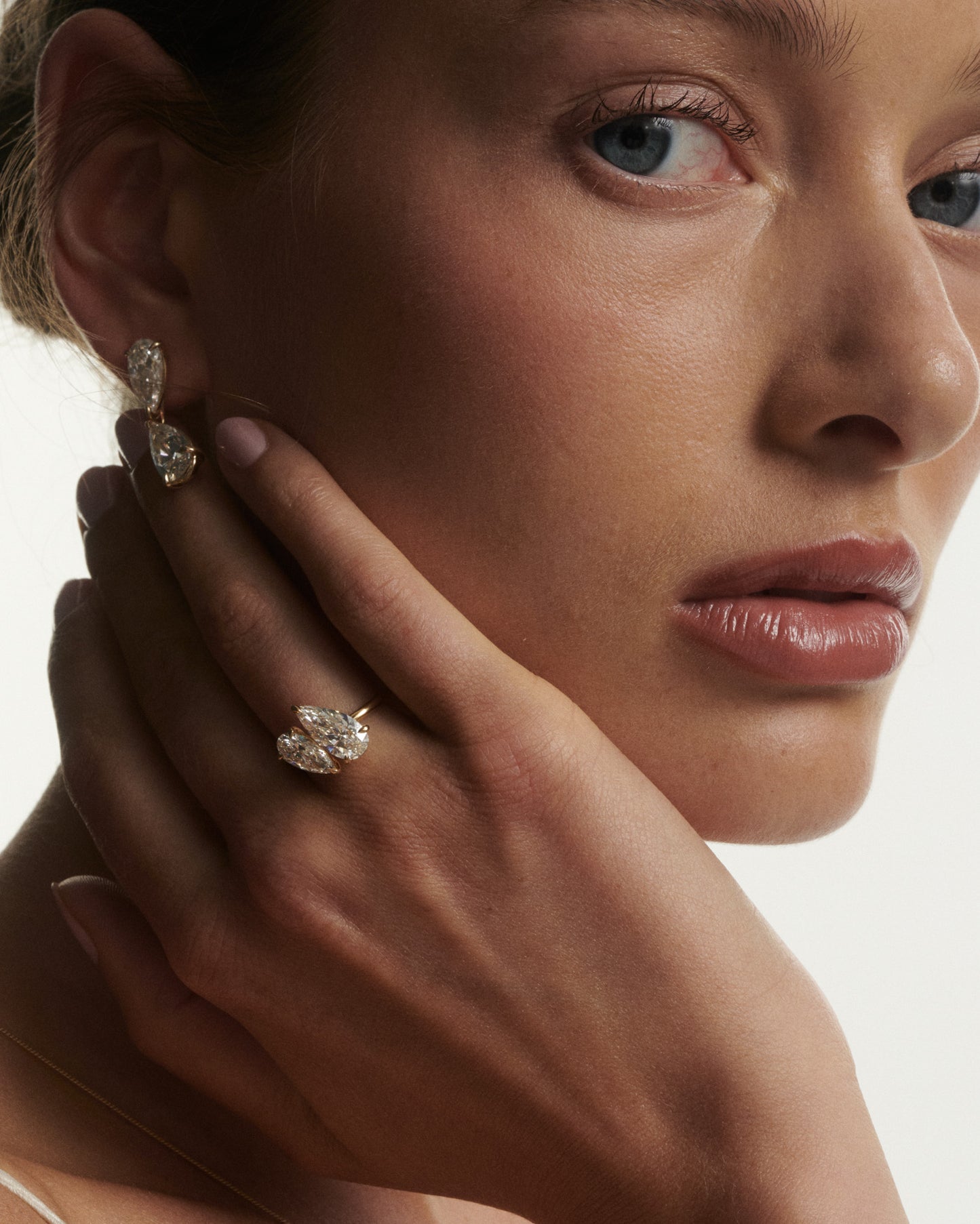 Close-up of a woman wearing diamond earrings with a neutral background