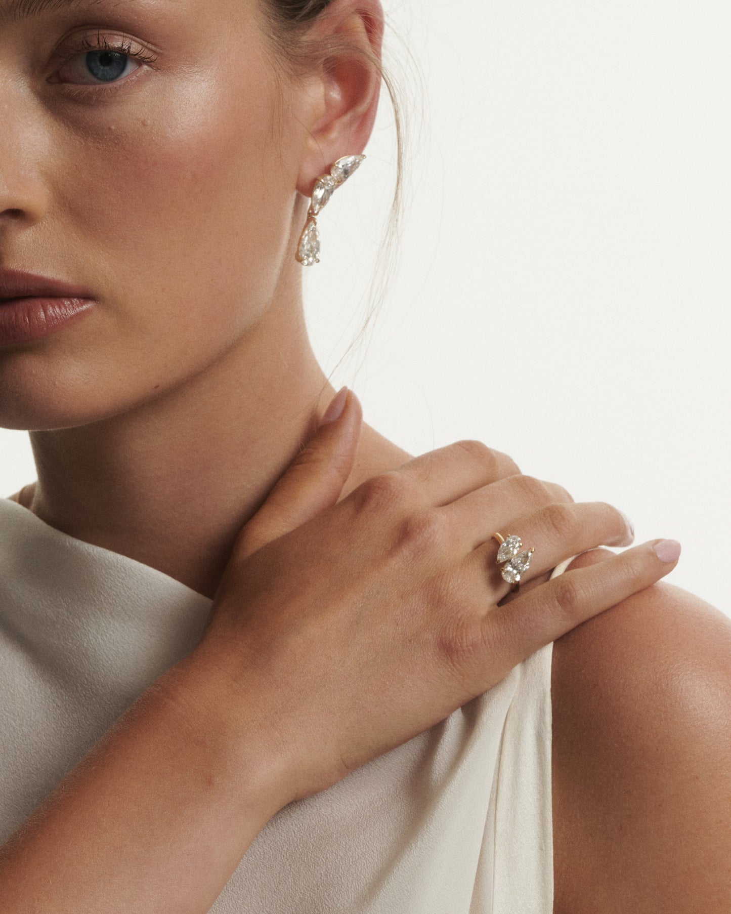 Close-up of a woman wearing a diamond ring and earrings on a neutral background