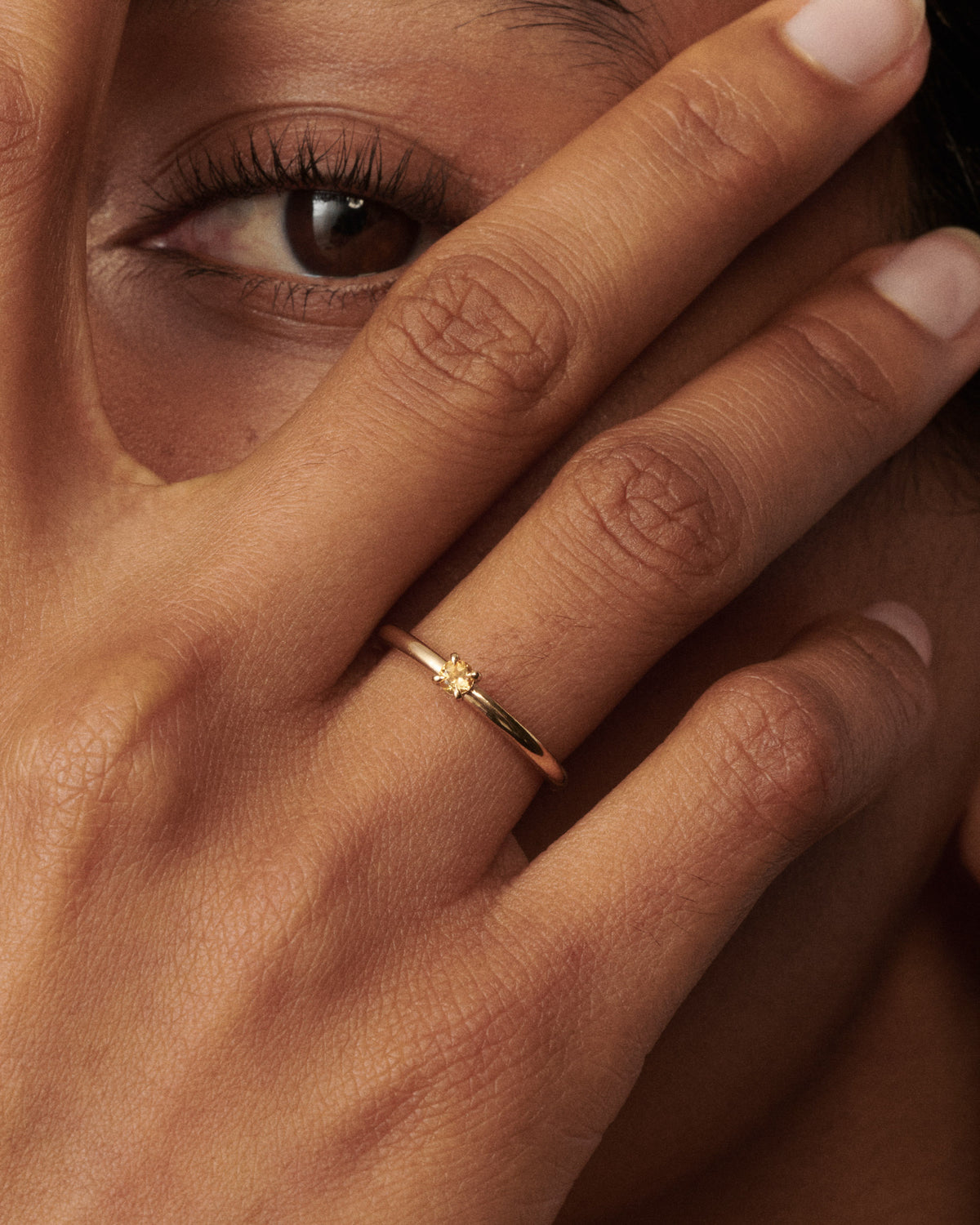Woman wear a citrine yellow gold birthstone ring up to her eye