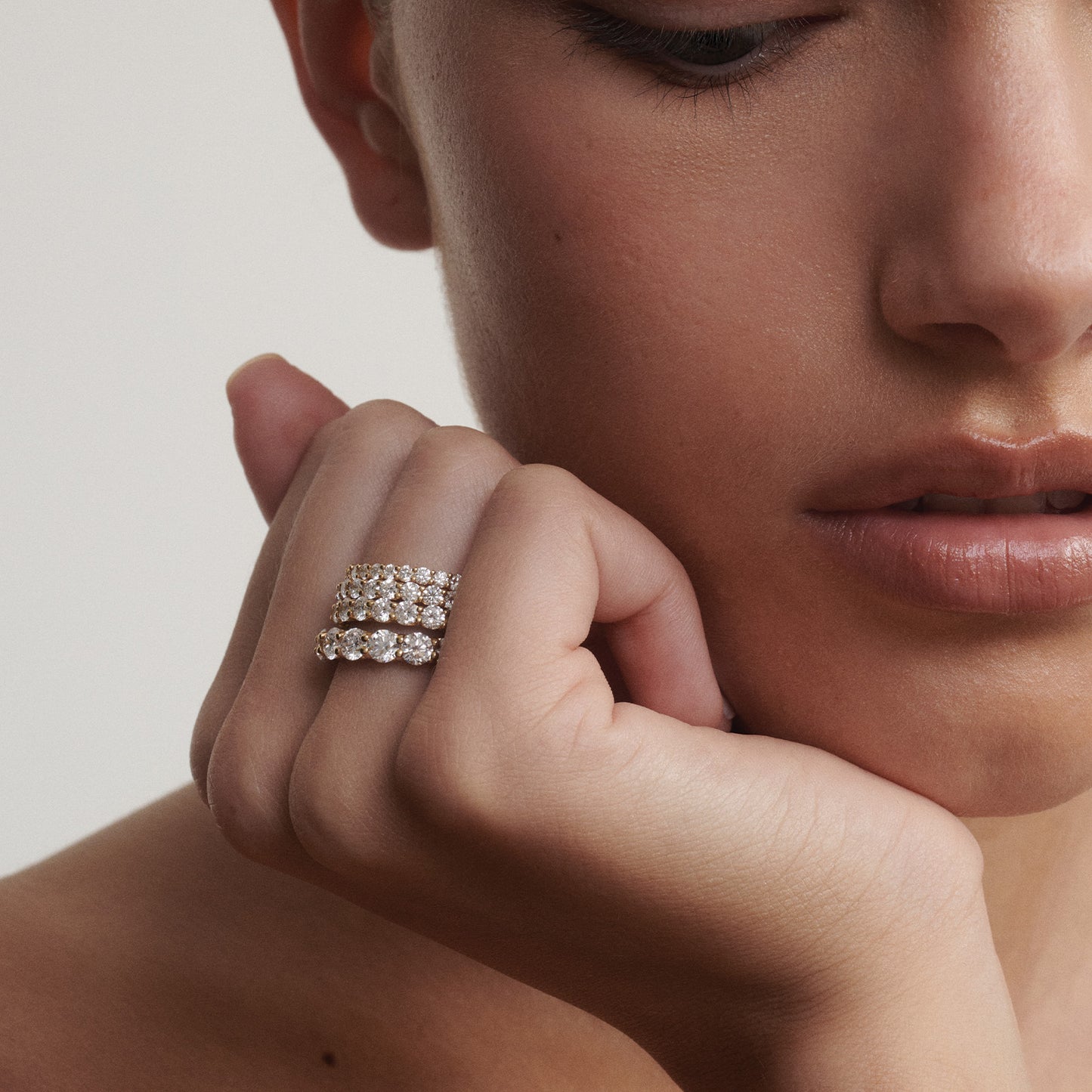 Close-up of a woman's hand wearing four diamond rings stacked on a neutral background