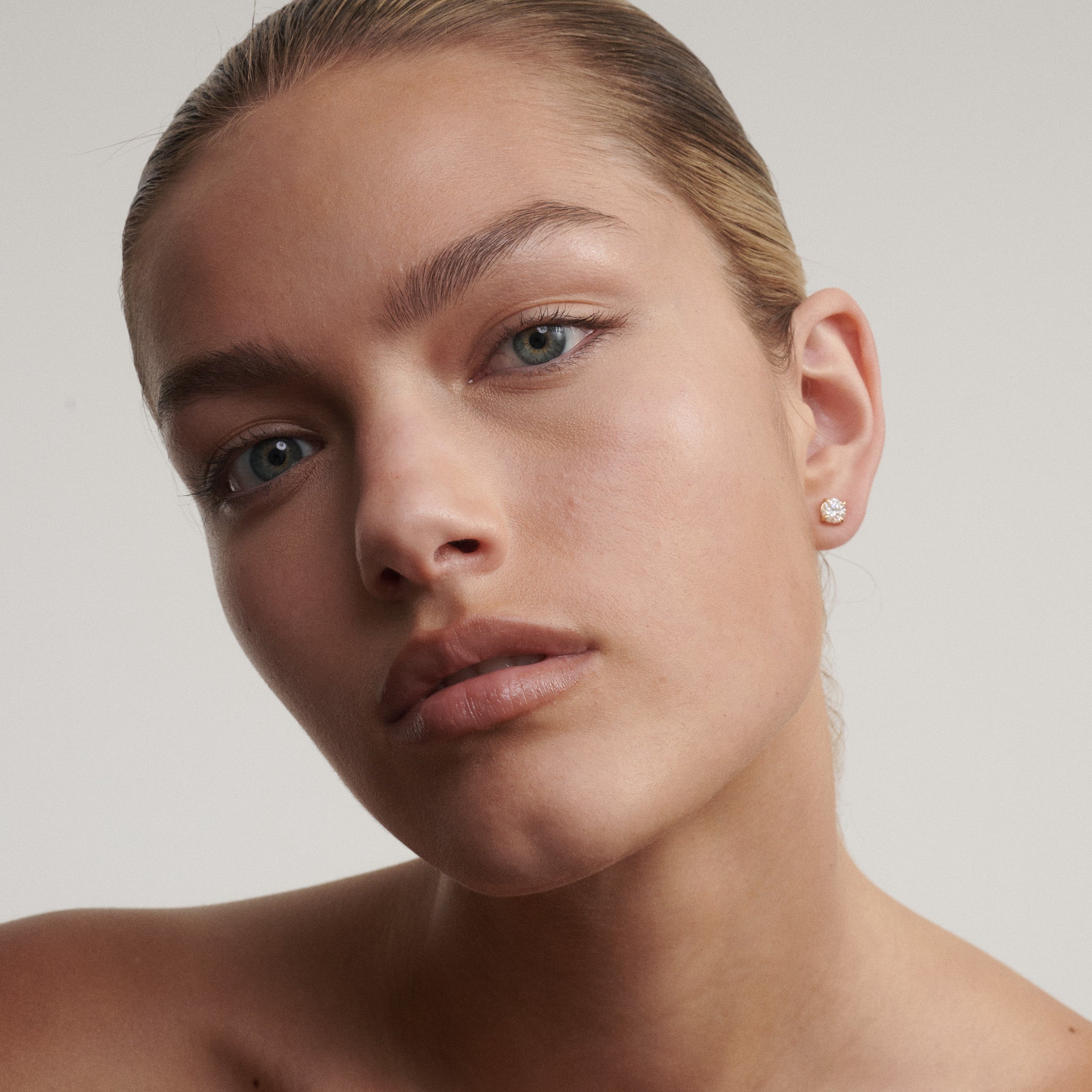Close-up of a woman's face wearing diamond earrings with a neutral background
