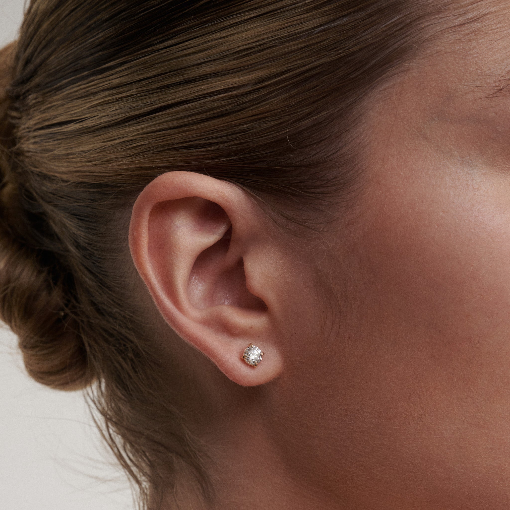 Close-up of an ear wearing a diamond earring with a neutral background