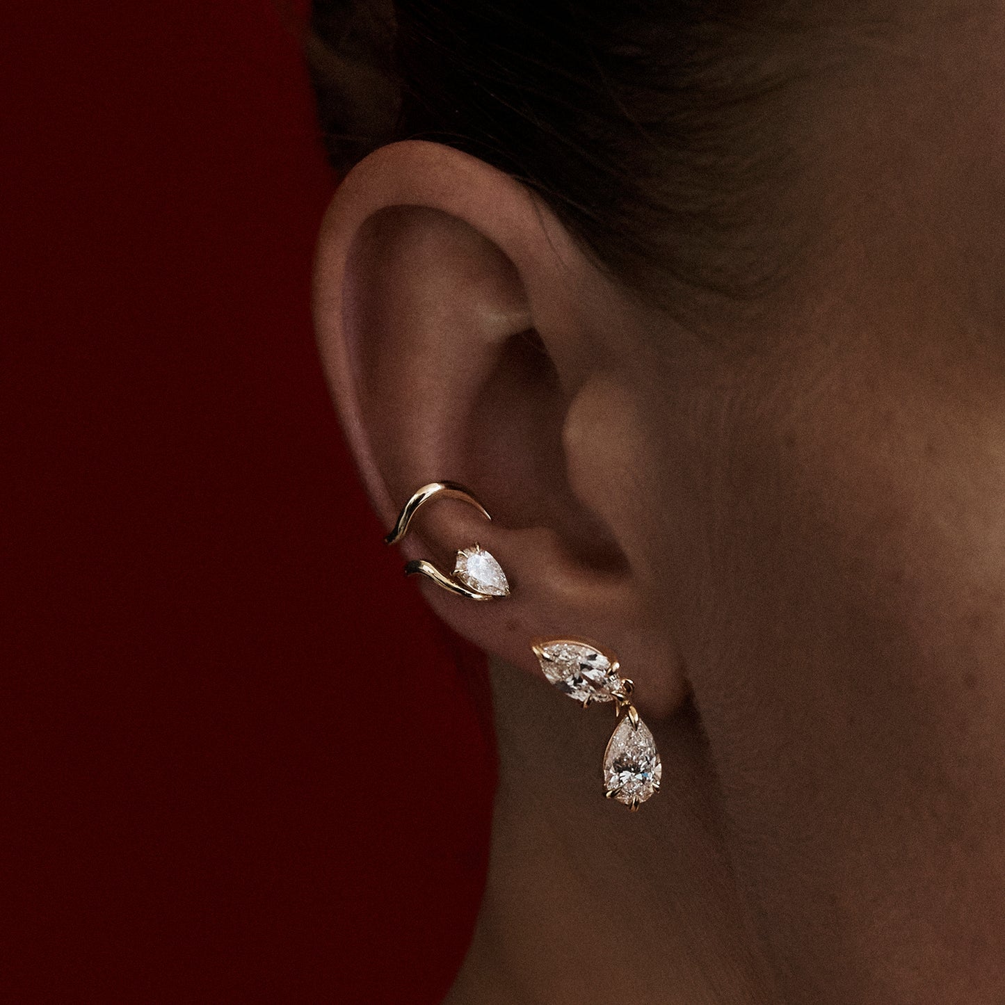 Close-up of an ear wearing gold earrings with a dark background