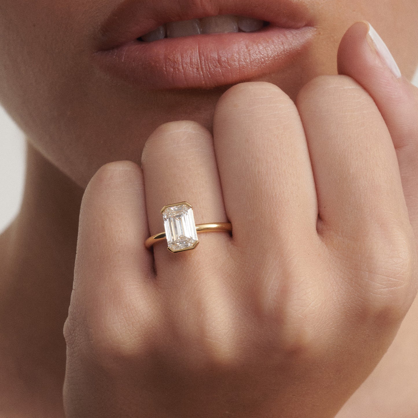 Close-up of a hand wearing a rose gold ring with a diamond, against a neutral background.