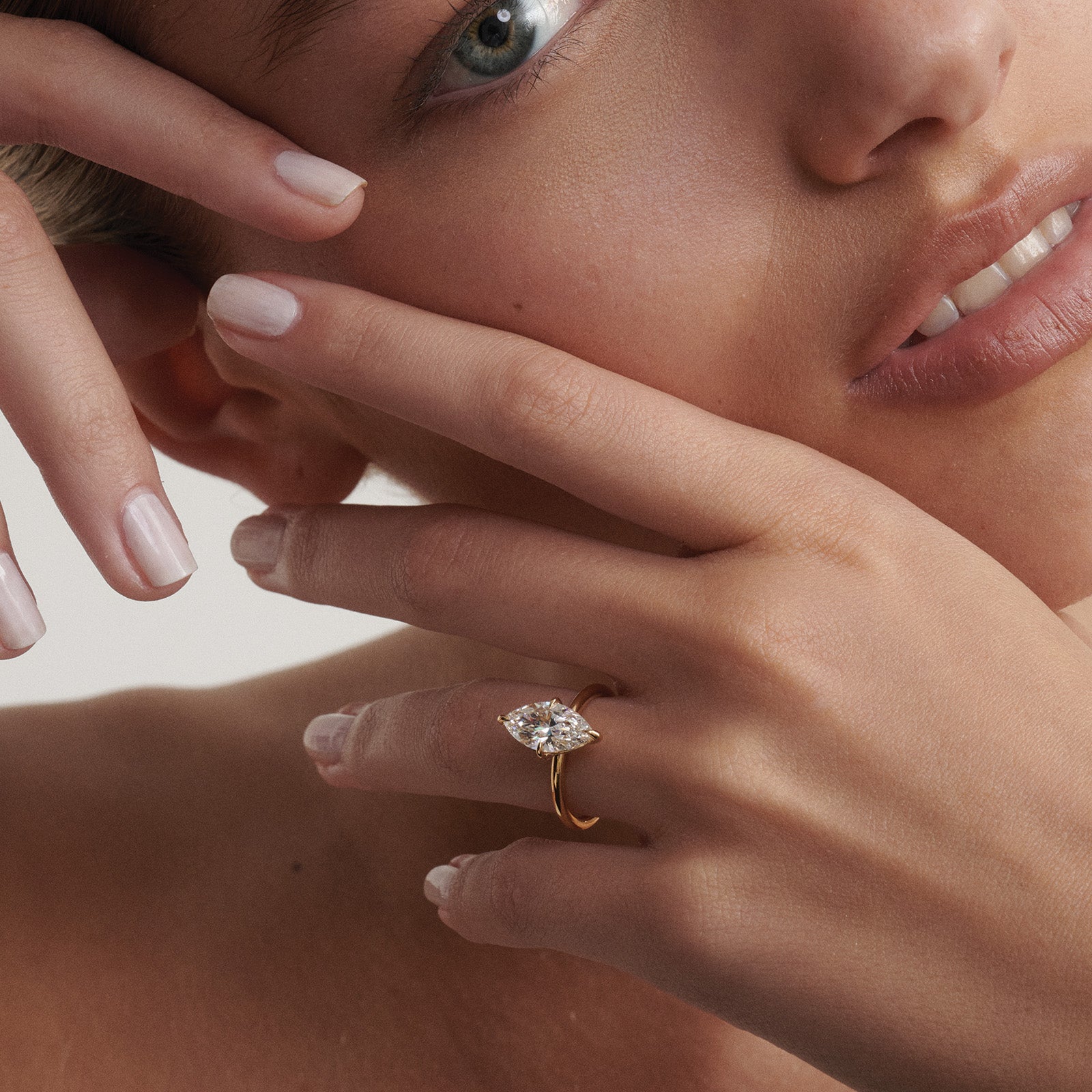 Close-up of a woman's hand wearing a gold ring with a diamond, touching her face.