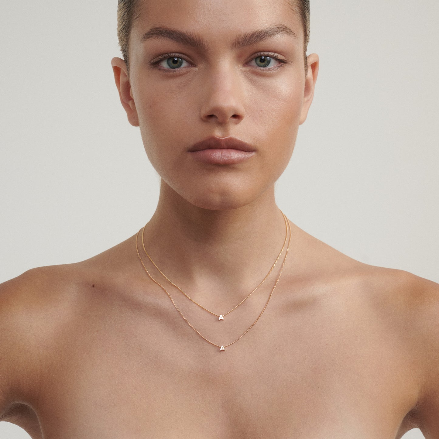 Woman wearing a delicate gold necklace with a triangle pendant on a neutral background