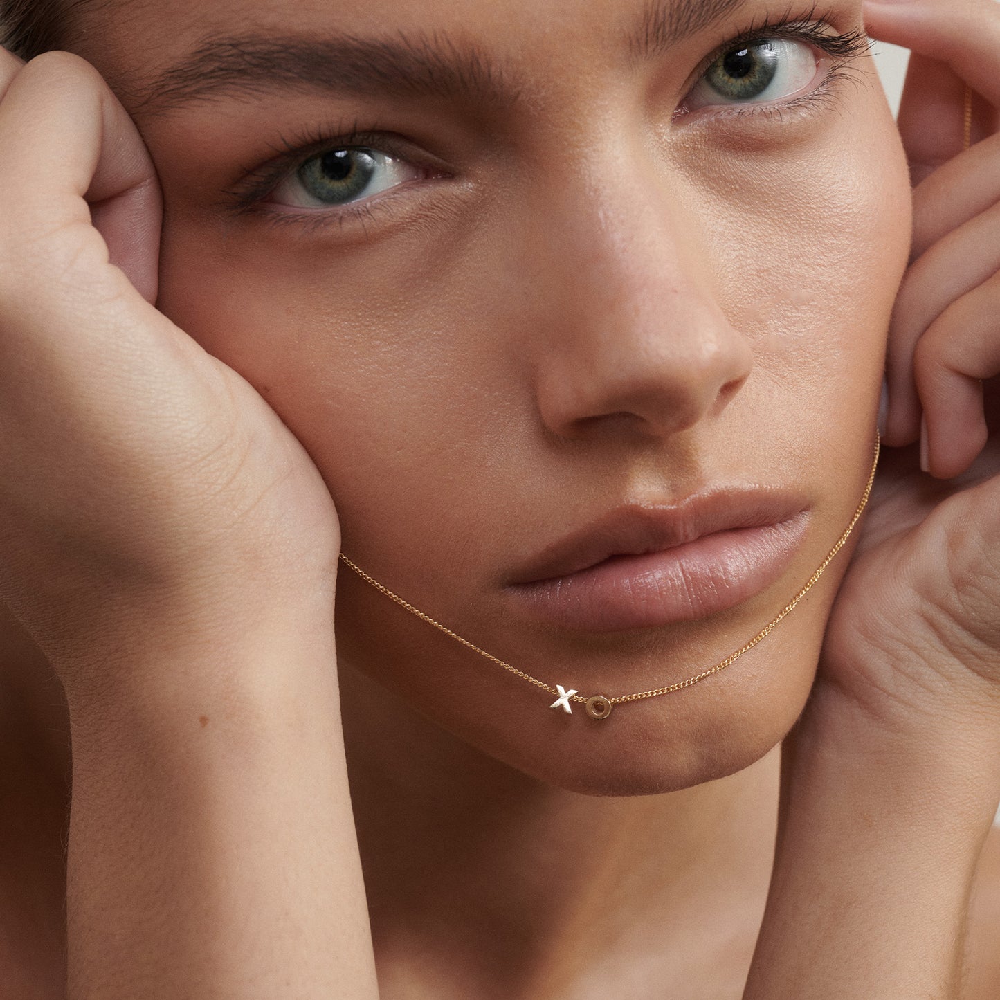 Close-up of a woman's face wearing a gold necklace with a X and O pendant.