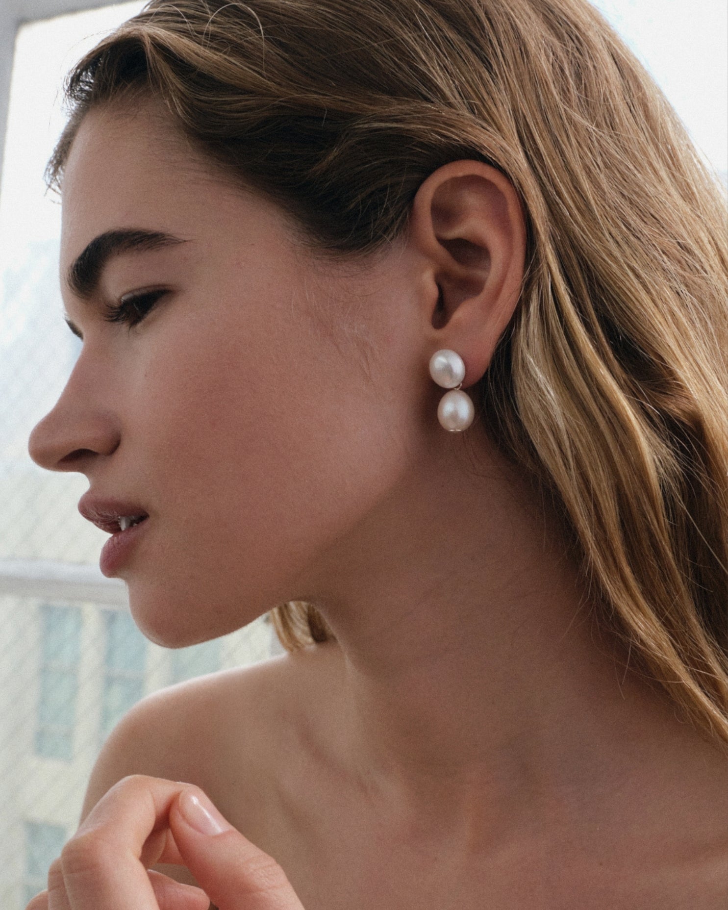 Close-up of a woman wearing pearl earrings with a display of heart-shaped engravable pendants on a white background.