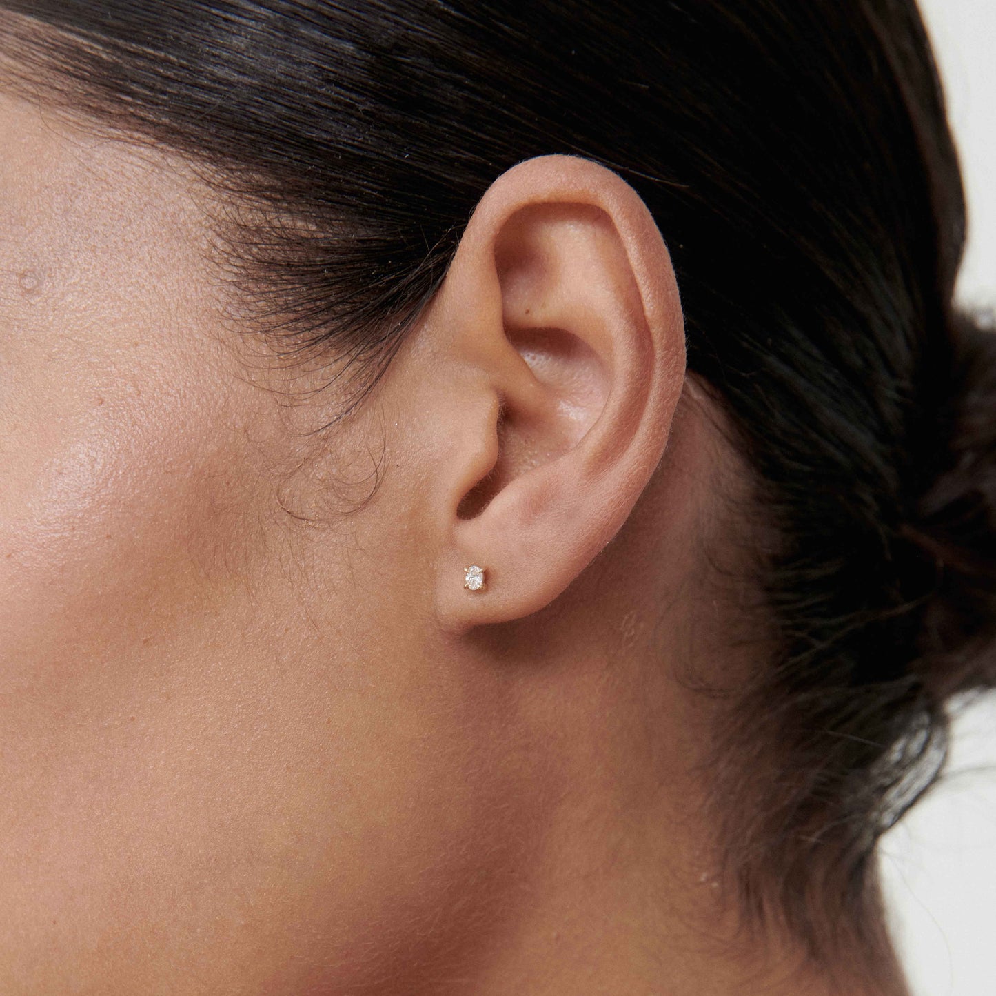 Close-up of a woman's ear wearing a small diamond stud earring, showcasing luxury jewellery. Minimalist and elegant design.