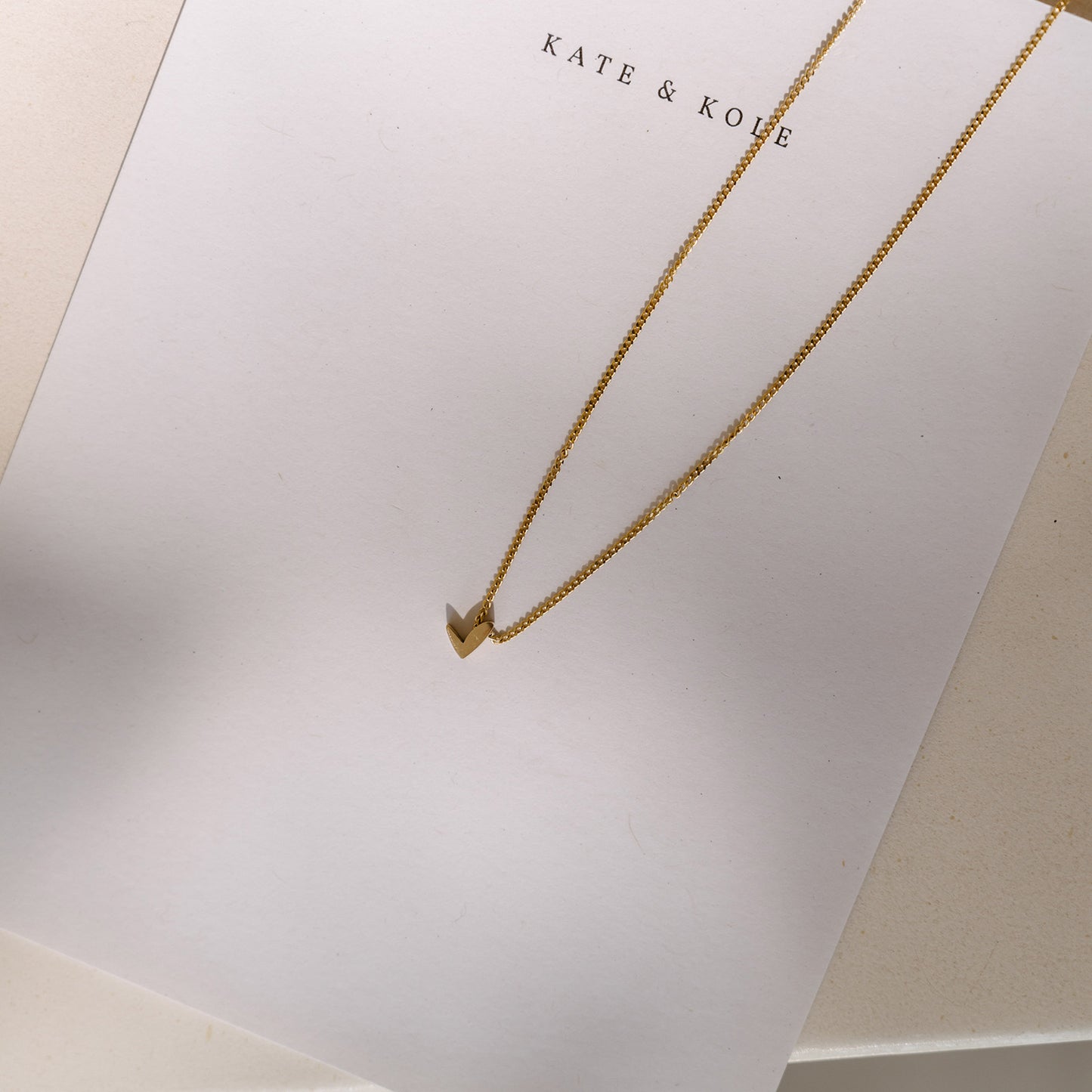 Elegant gold necklace with a small V-shaped pendant on KATE & KOVE branded paper, highlighting luxury jewellery design.