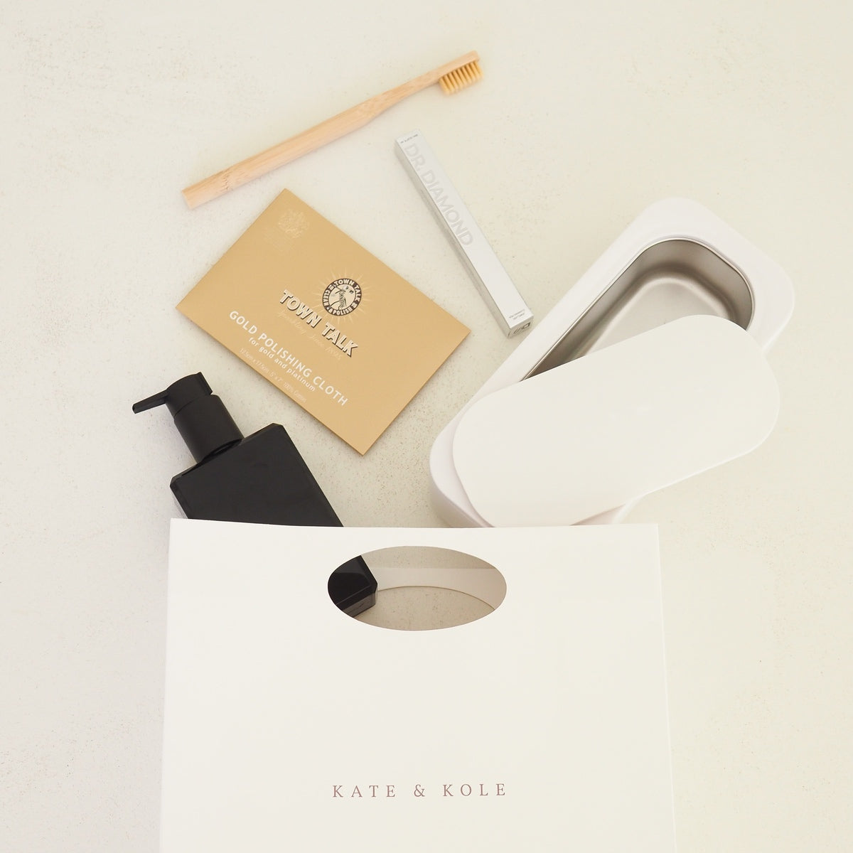 Cleaning products including a black bottle, beige box, and white brush on a light surface with 'KATE & KOLE' branding.