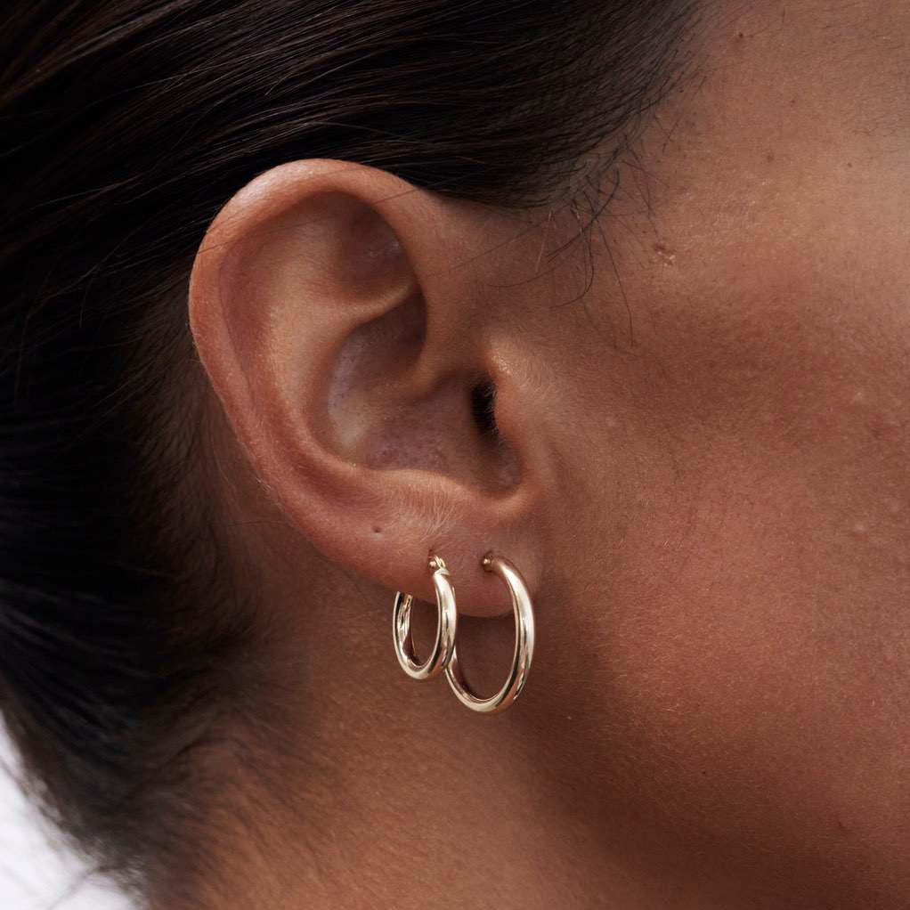 Close-up of a woman's ear wearing two sleek gold hoops, highlighting luxury jewellery fashion.