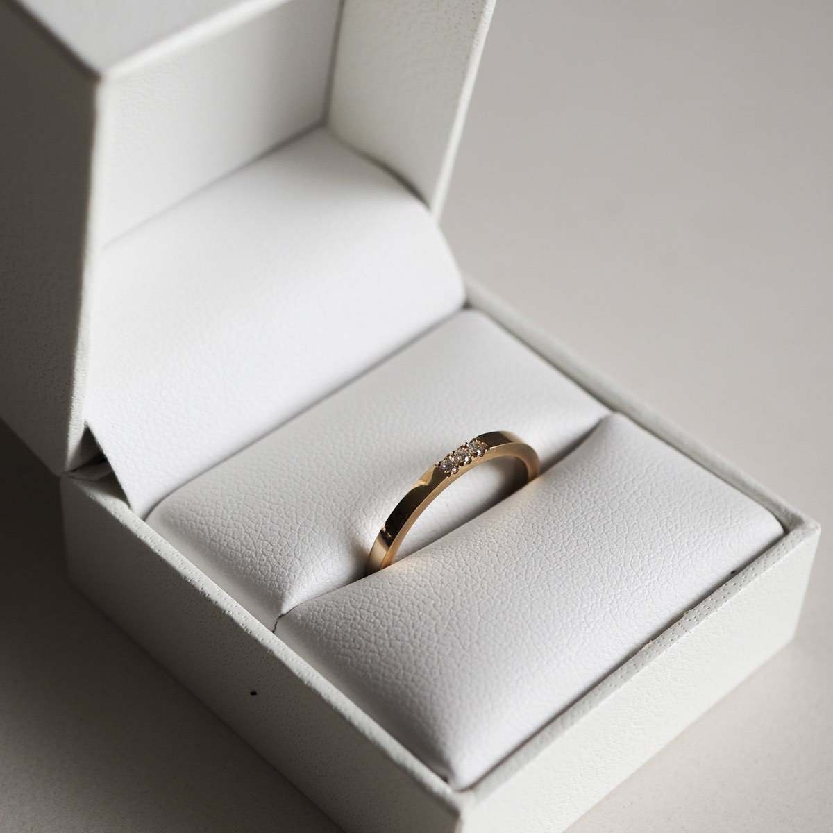 Gold ring with small diamonds in a white jewellery box, capturing luxury and elegance. Perfect for weddings or special occasions.