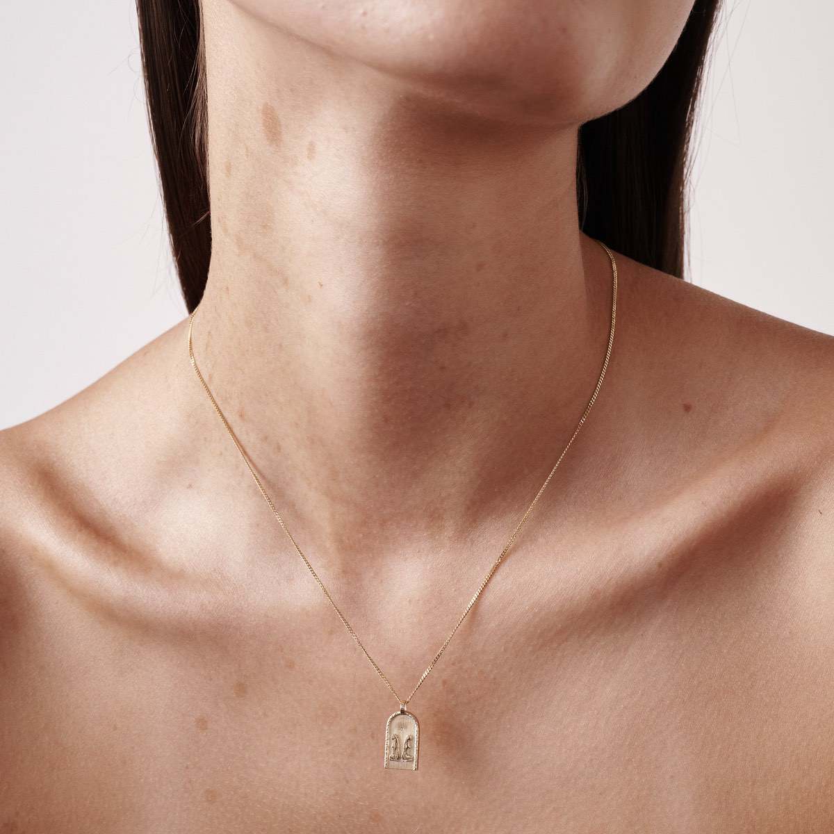 Minimalist gold necklace with arch-shaped pendant worn by a woman. Elegant jewellery design highlights luxury and simplicity.