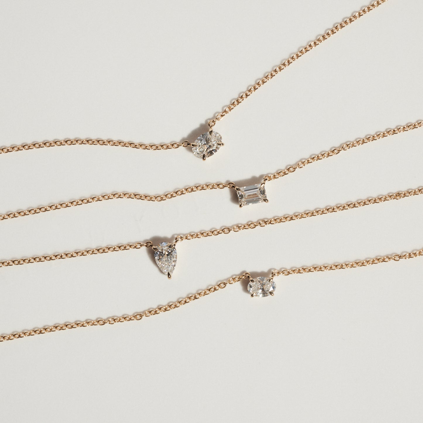 Set of gold necklaces with various diamond pendants on a light gray background