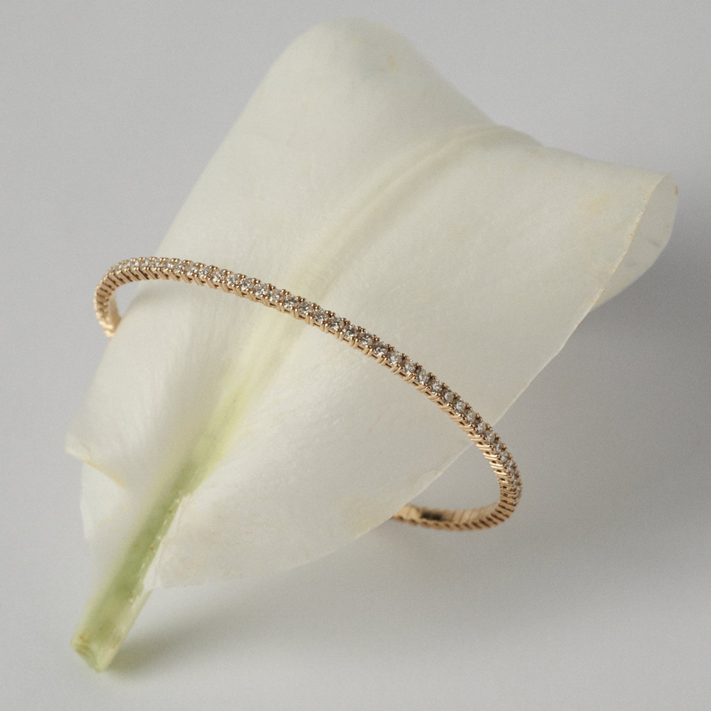 Gold bracelet with diamonds on a white petal against a light gray background