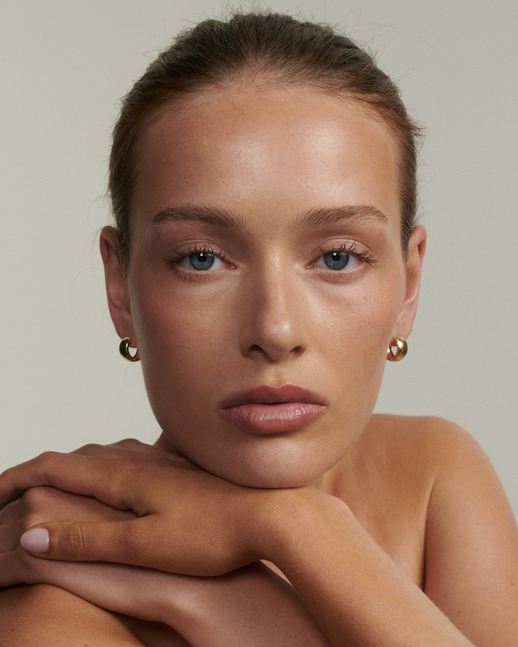 Woman wearing gold hoop earrings against a plain background