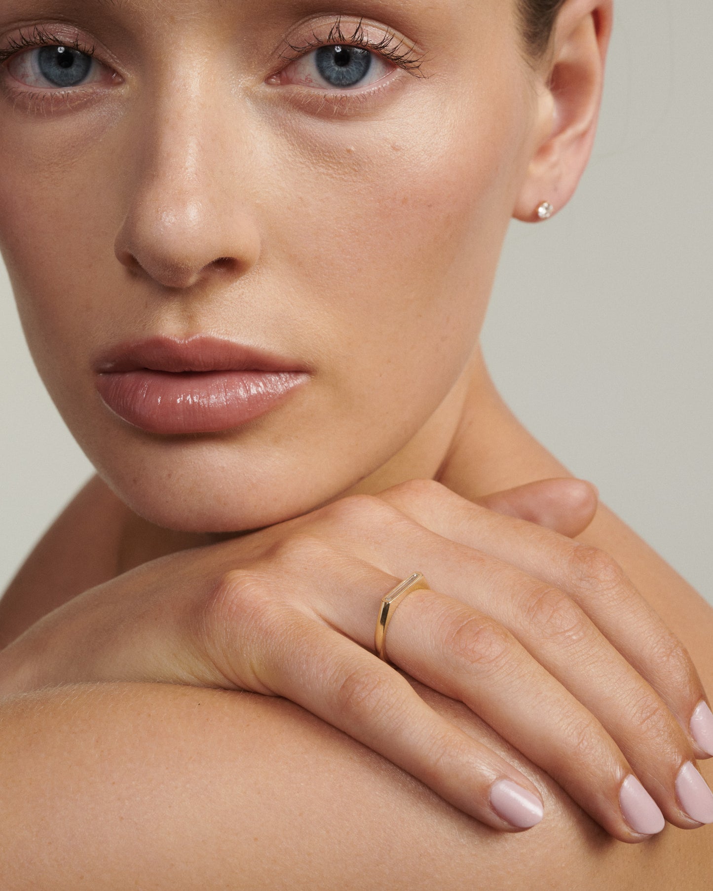 Close-up of a woman's face with a gold ring on her finger, against a neutral background
