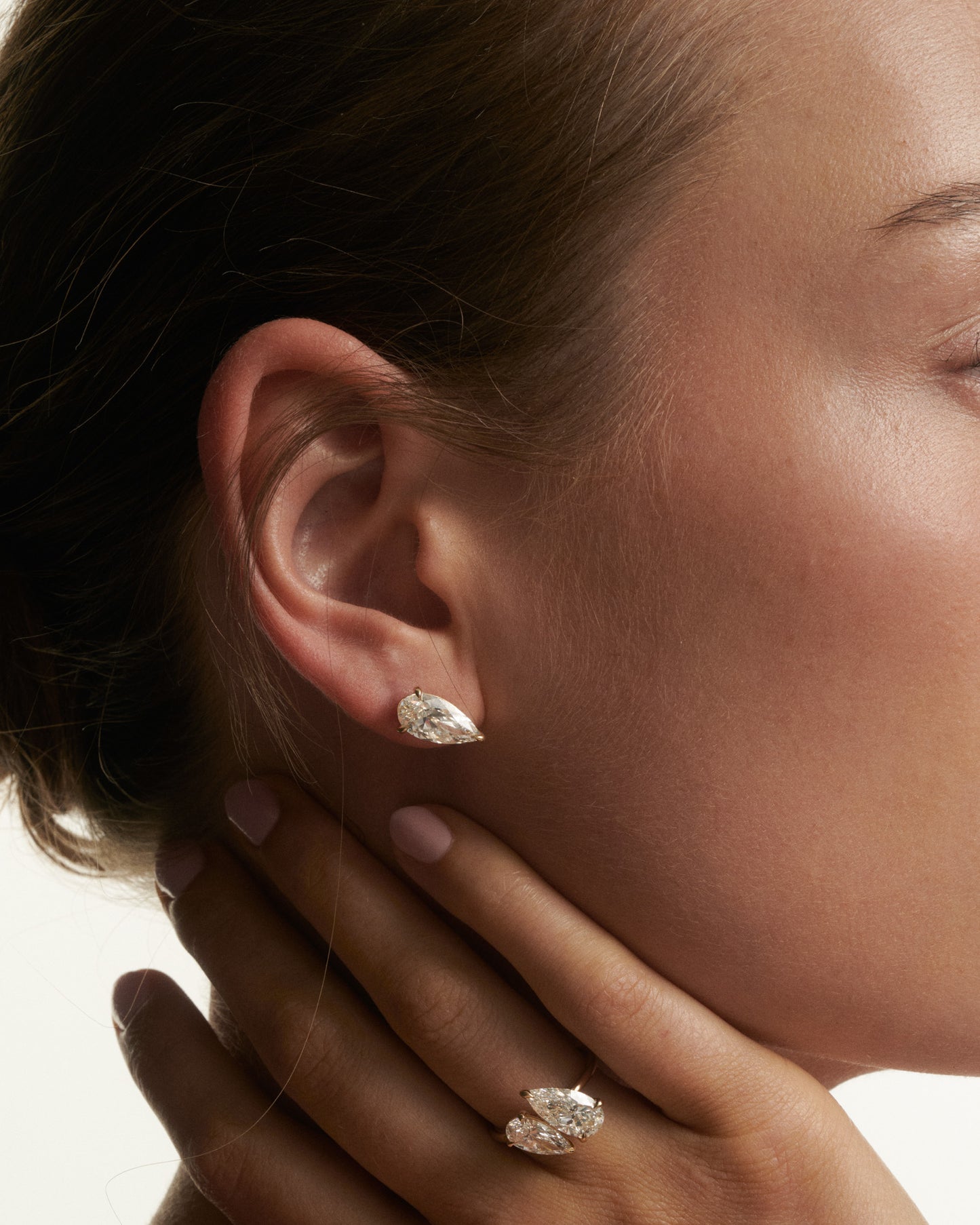 Close-up of a woman wearing diamond earrings with a hand touching her face.