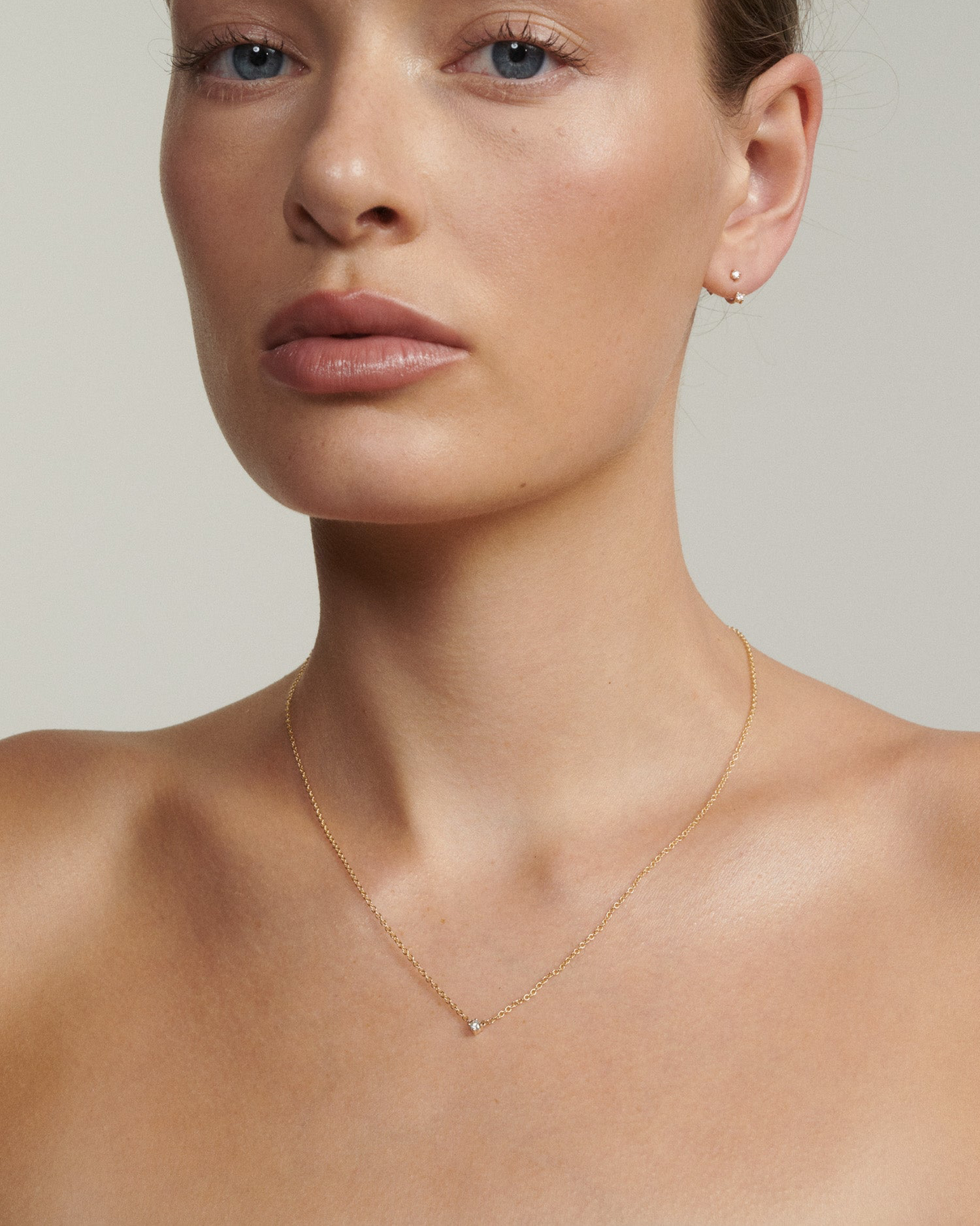 Close-up of a person wearing a delicate gold necklace against a neutral background