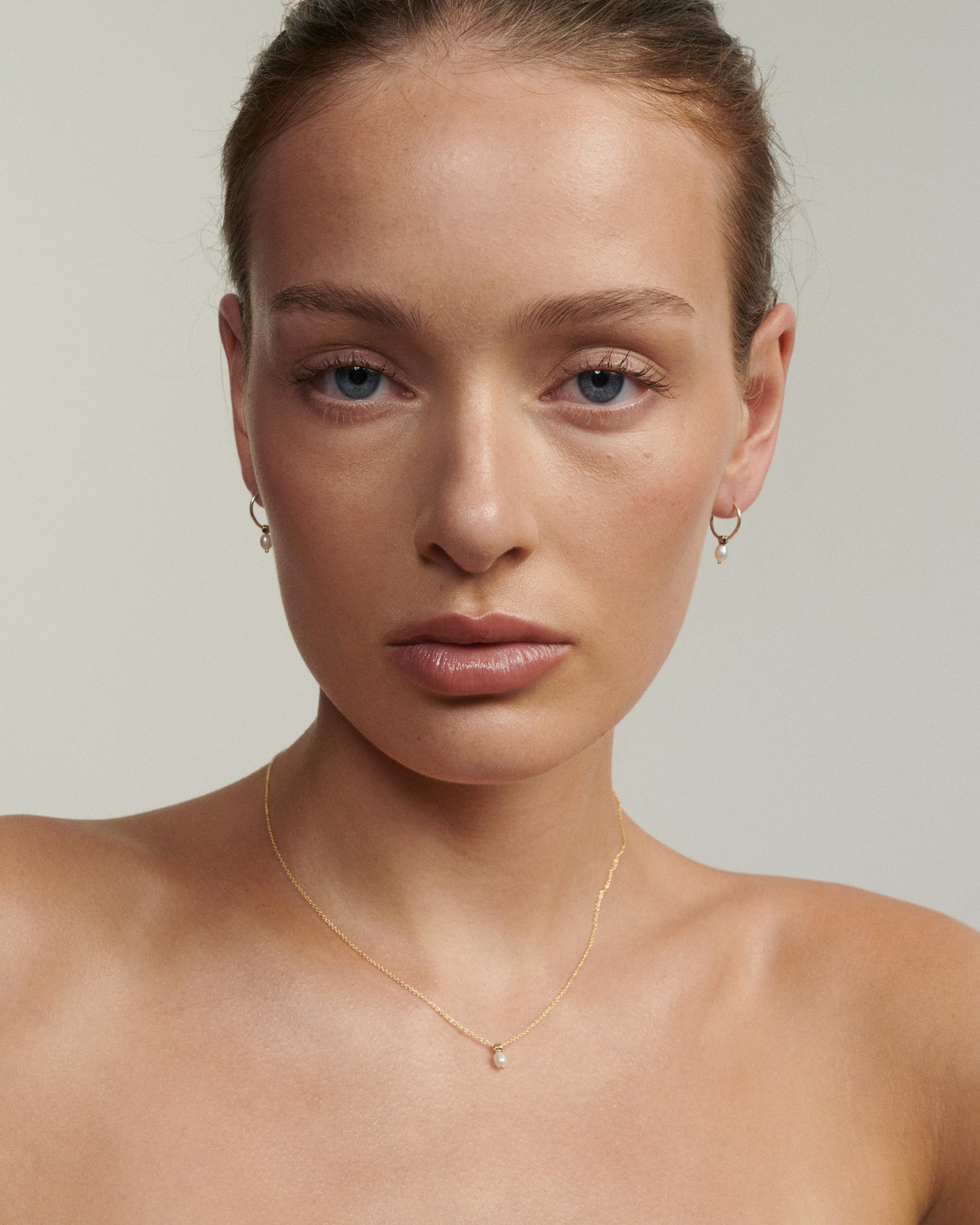 Woman wearing a gold necklace and earrings against a neutral background