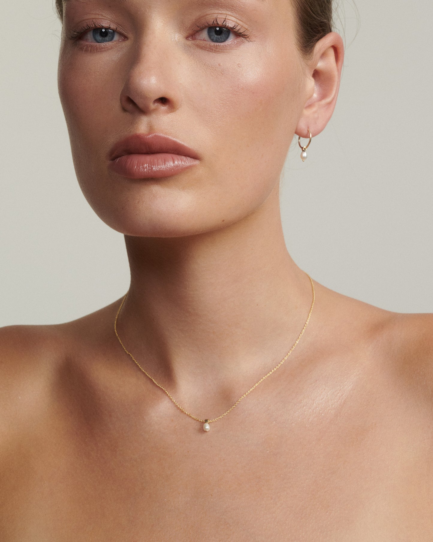 Close-up of a woman wearing a gold necklace and earring on a neutral background