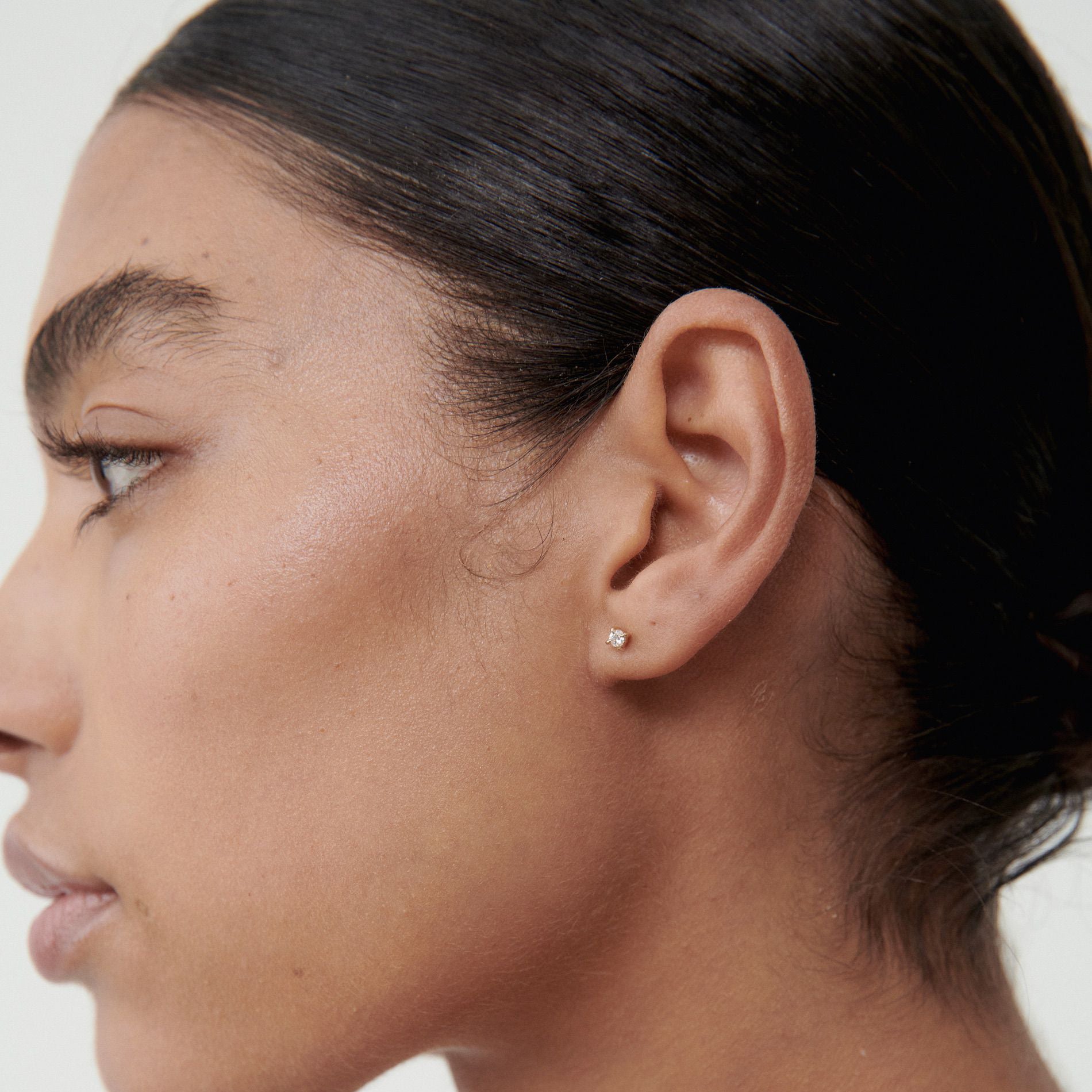 Close-up of a person's ear with an earring on a neutral background