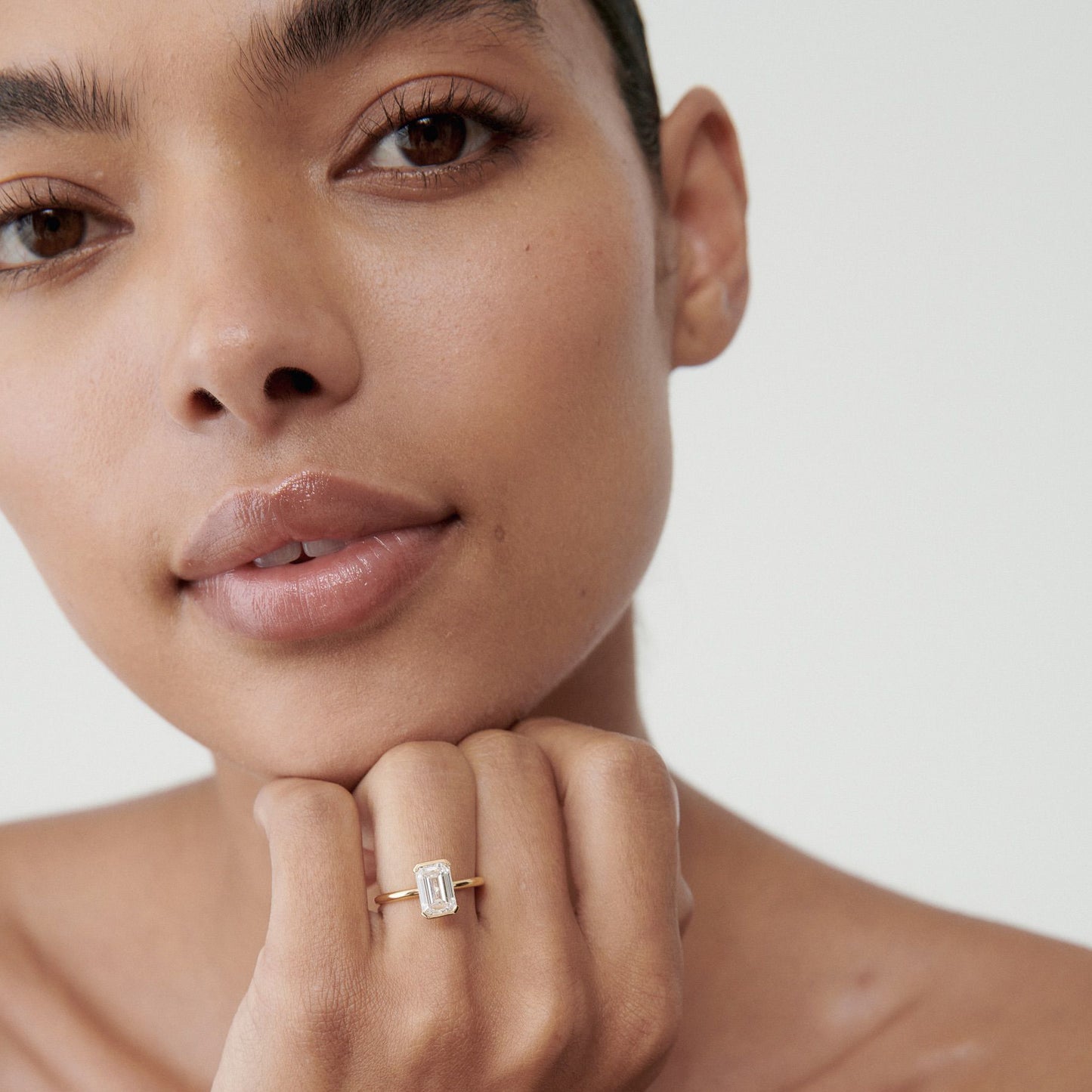 Woman showcasing an emerald-cut diamond ring on her finger. Close-up, minimalistic, luxury jewellery focus. [text overlay: 2ct Diamond]