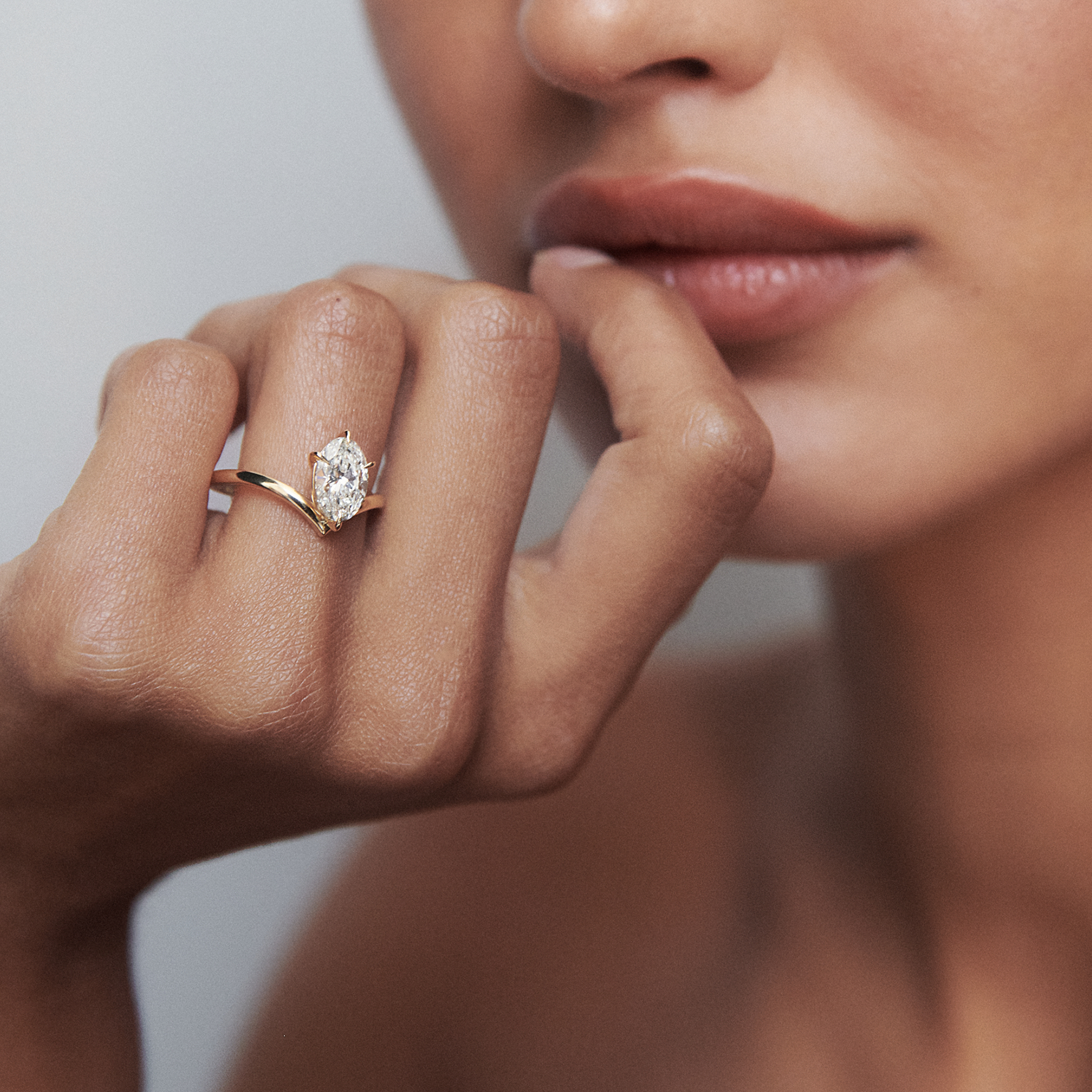 Close-up of a person wearing an elegant gold ring with a marquise-cut diamond, subtly posed near their lips, highlighting luxury jewellery.