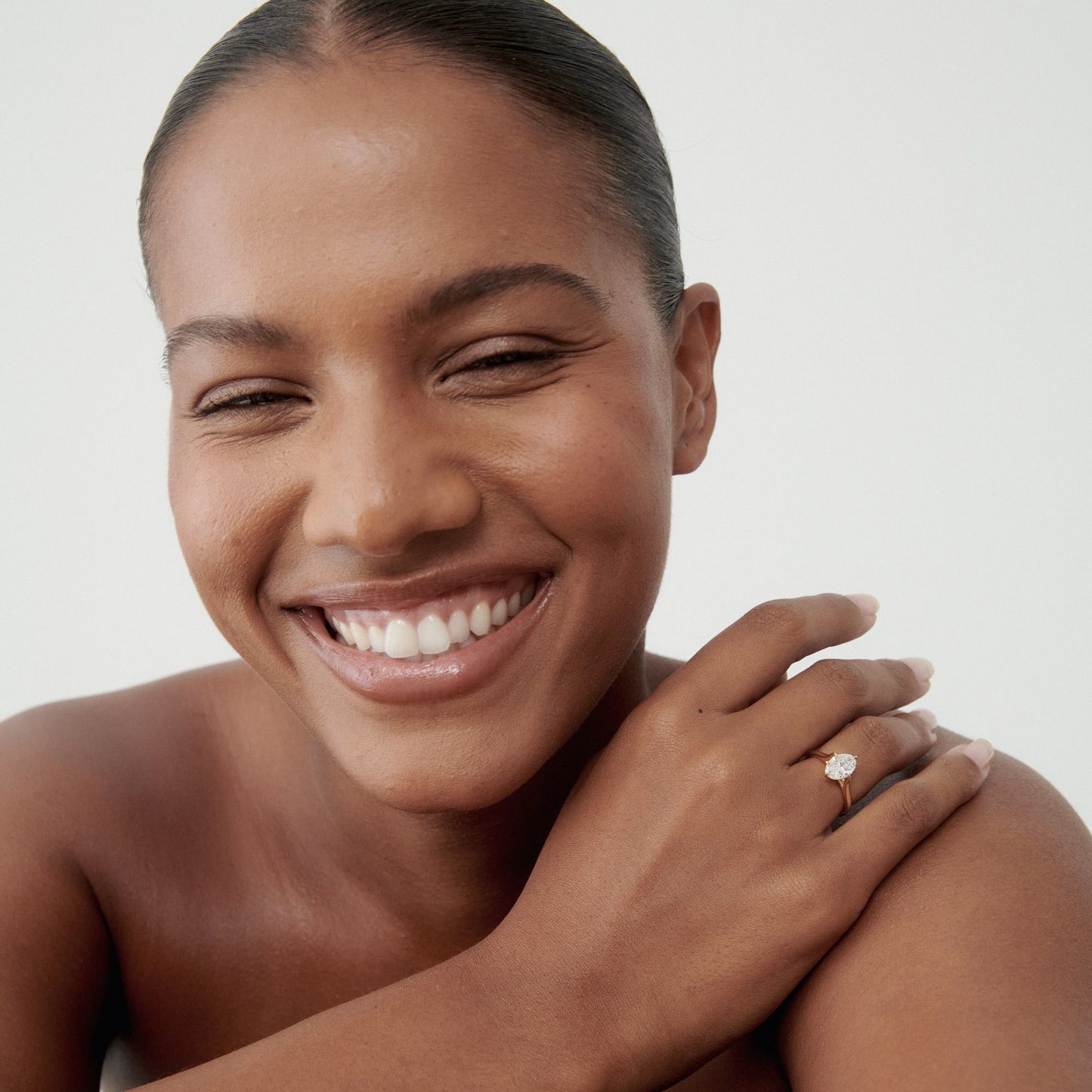 Smiling woman wearing a solitaire diamond ring. Hair tied back, showing confidence and elegance. Perfect for luxury jewellery marketing.