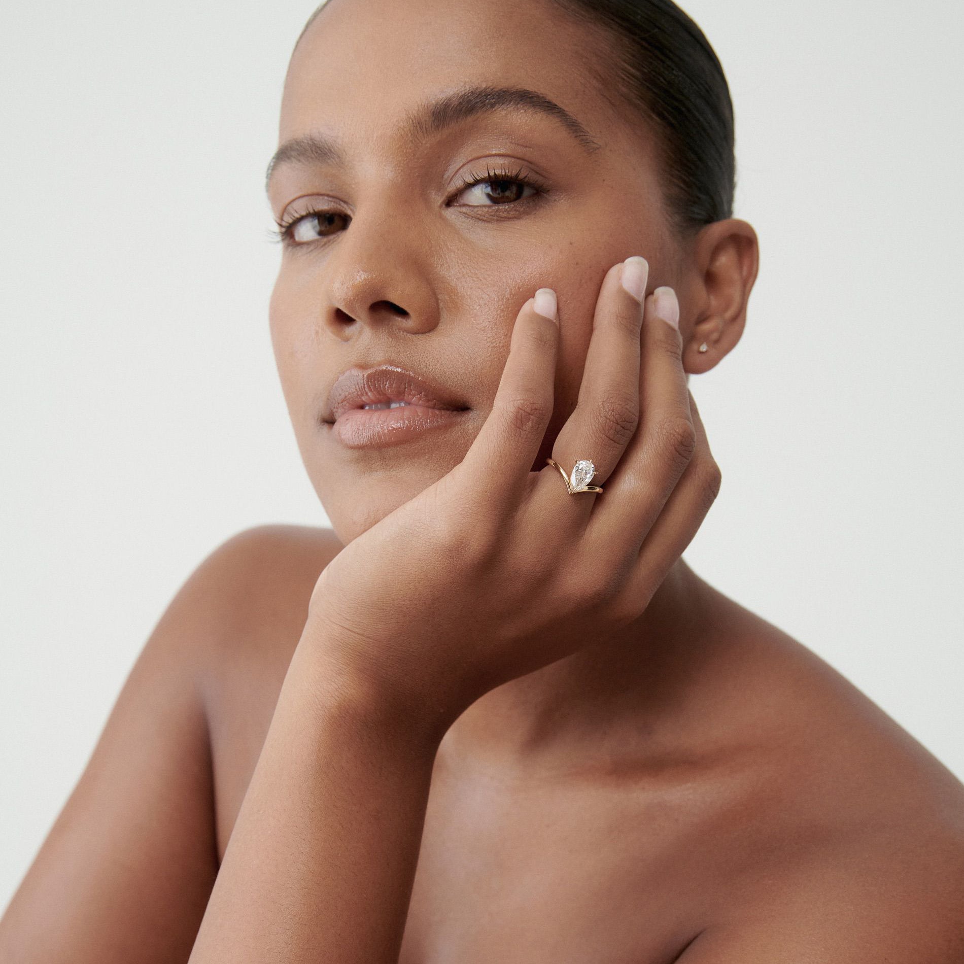Woman with sleek hair showcases a luxurious gold ring adorned with a large, clear gemstone. Elegant and minimalist jewellery style.