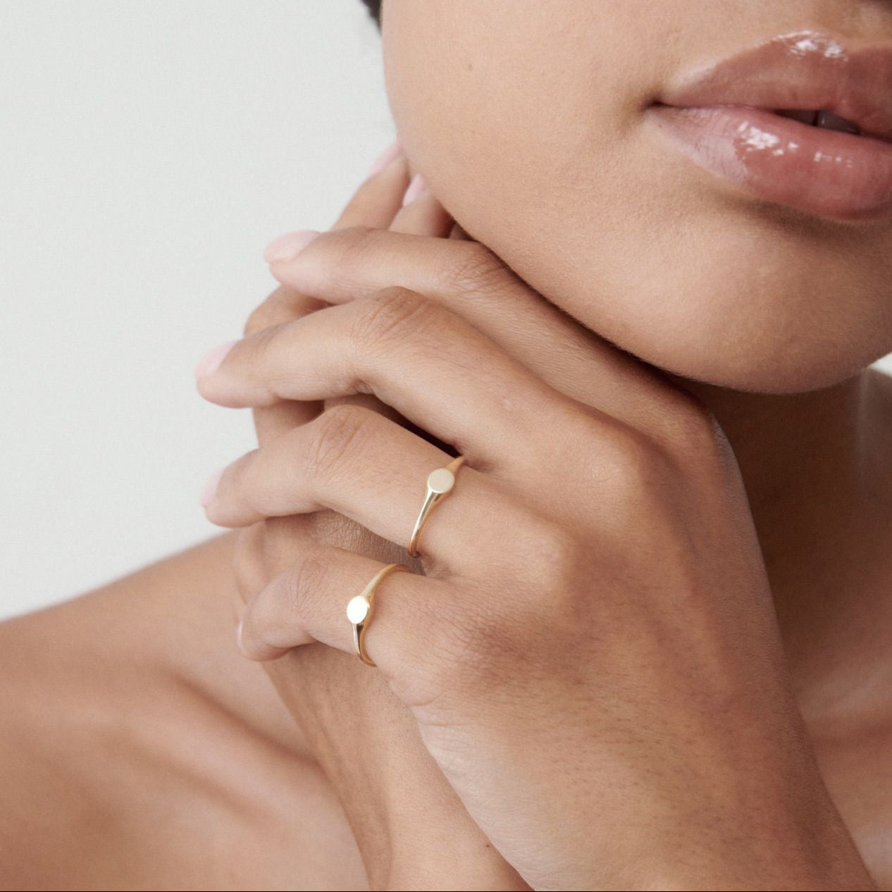 Woman with glossy lips and bare shoulders wearing a minimalist gold ring.