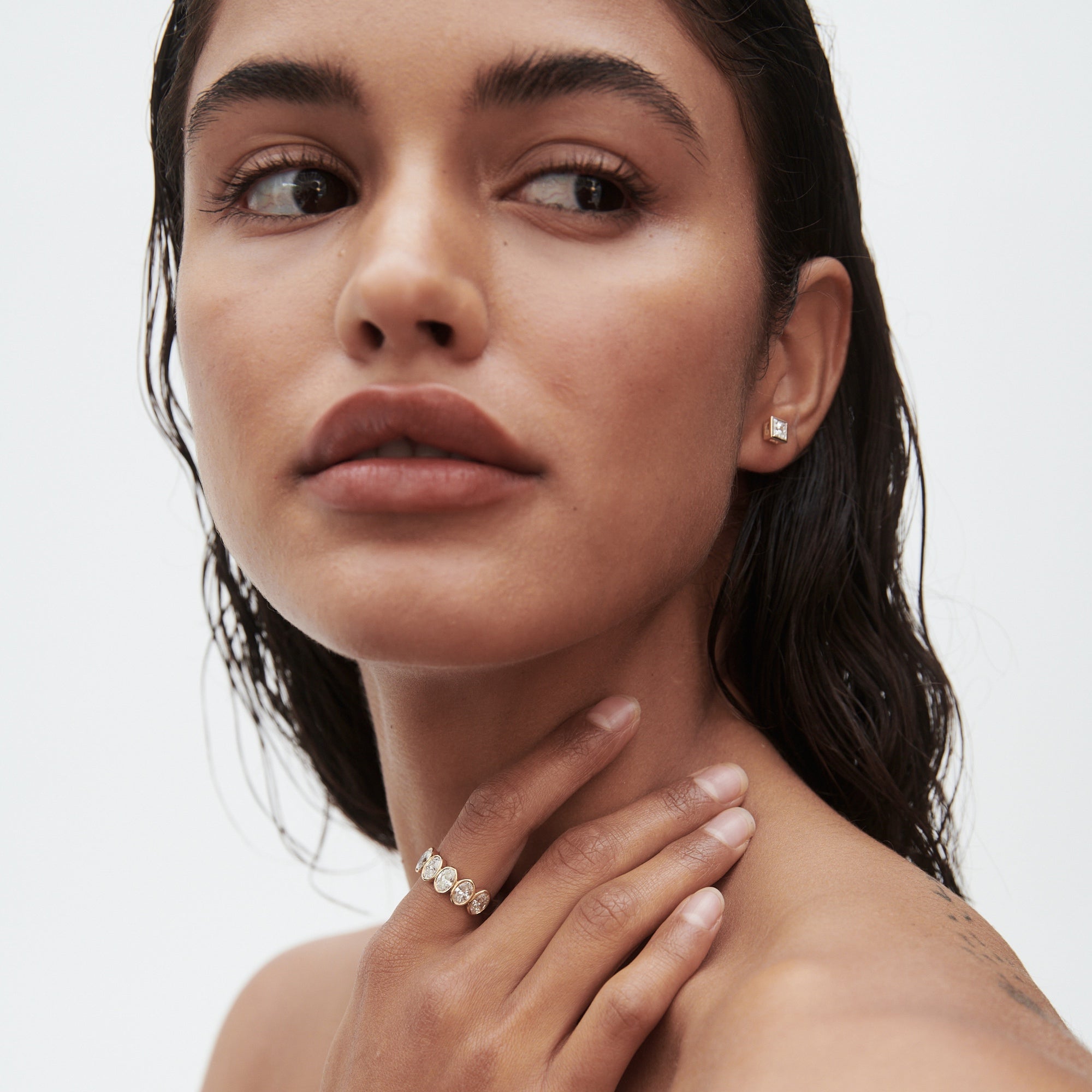Woman with wet hair wears diamond earrings and a statement ring, gazing to the side. Luxury jewellery, elegant and minimalist style.